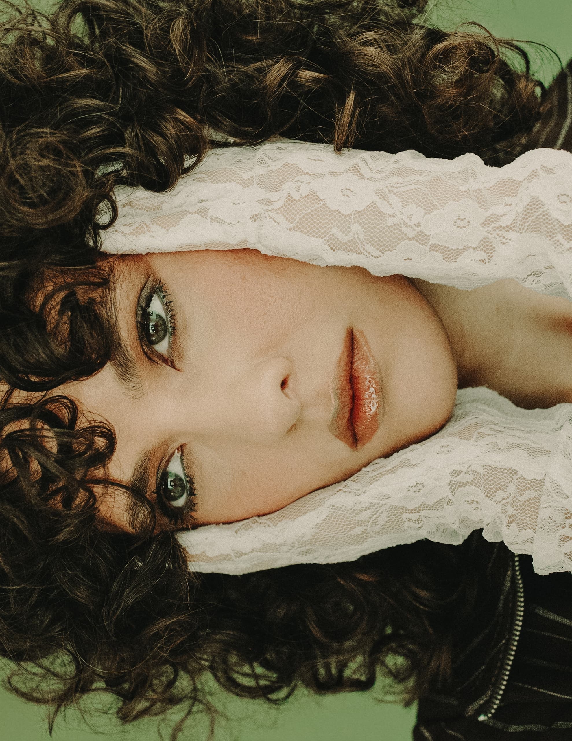 Close-up of a person with curly hair surrounded by white lace fabric.