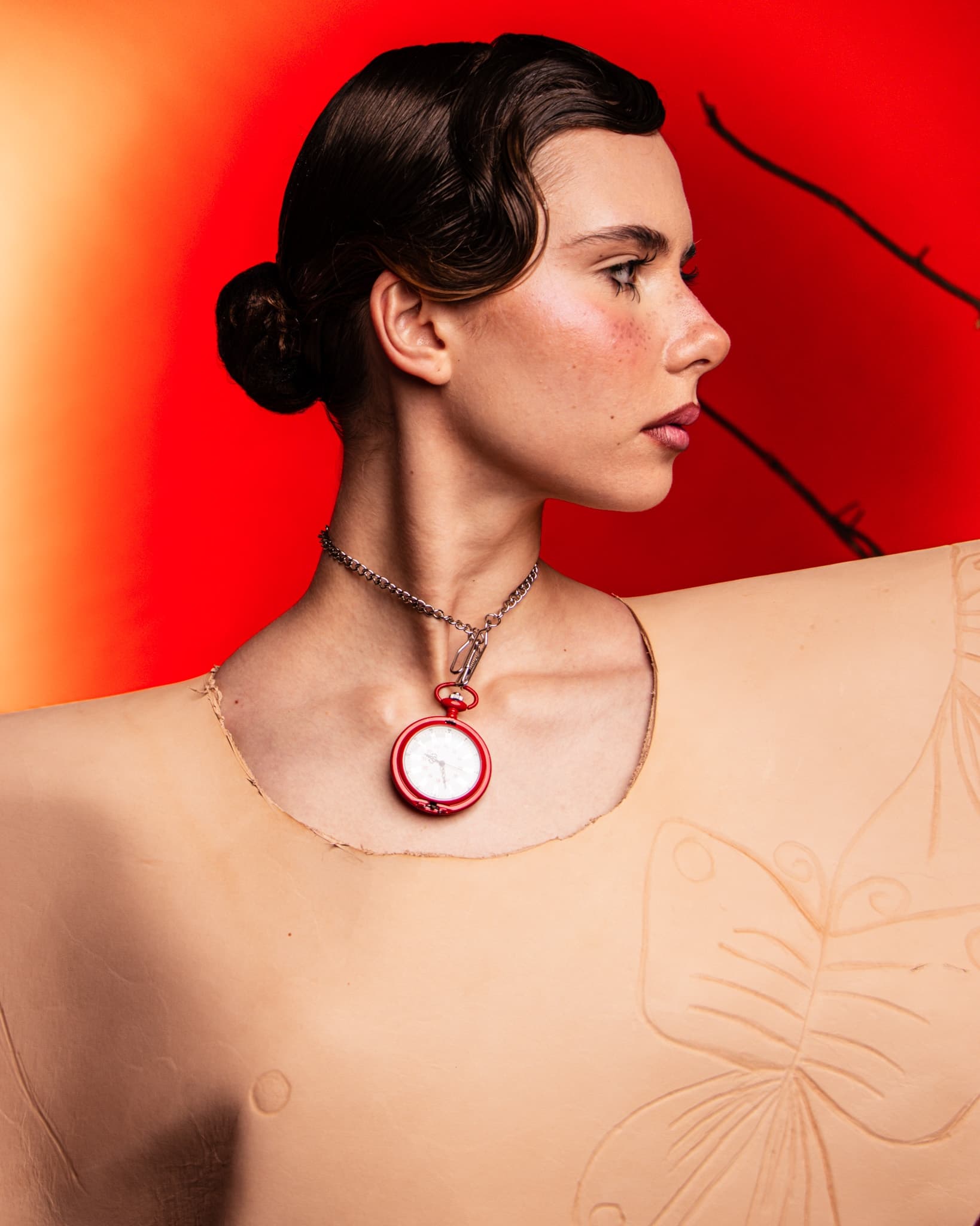 Profile portrait with vintage clock pendant, vibrant red background.