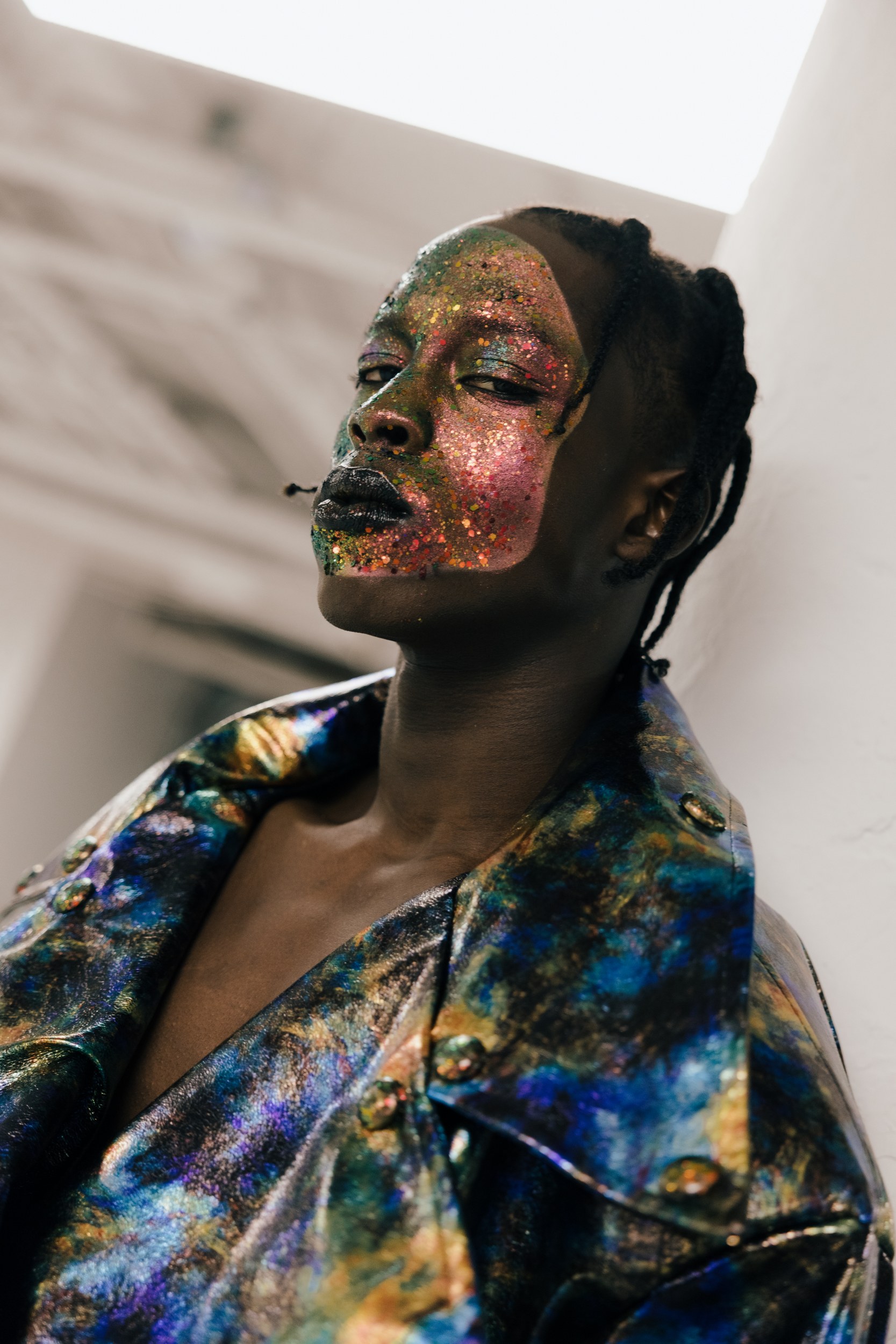 Person with glittery face paint and vibrant metallic jacket, looking upward confidently.