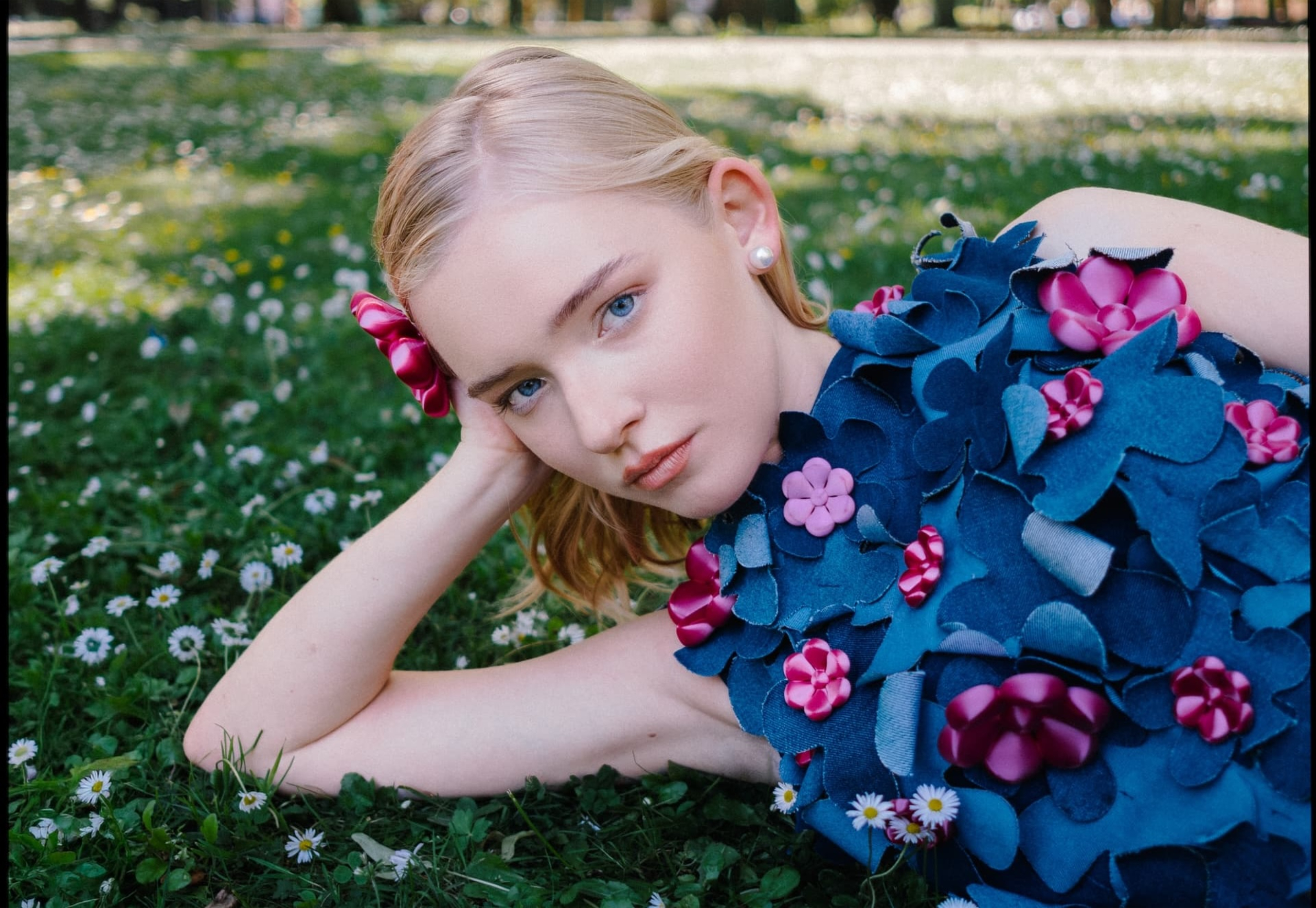 Person lying on grass in floral dress, surrounded by flowers.