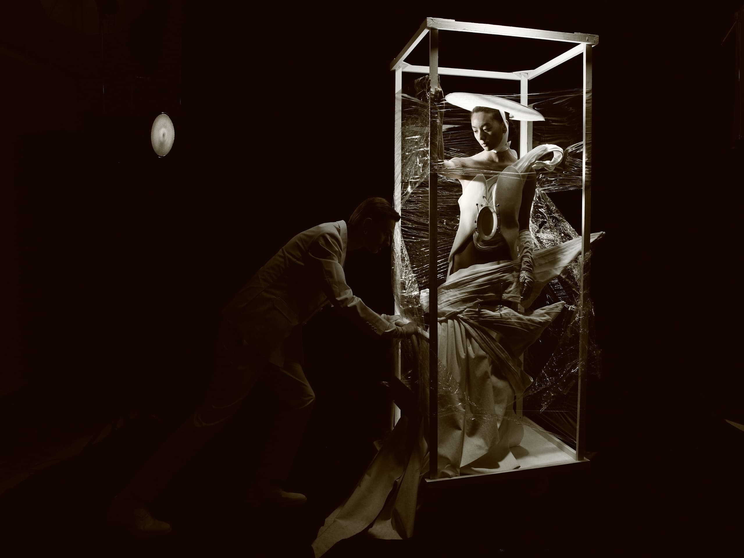 Avant-garde fashion art installation with figure in illuminated display case.