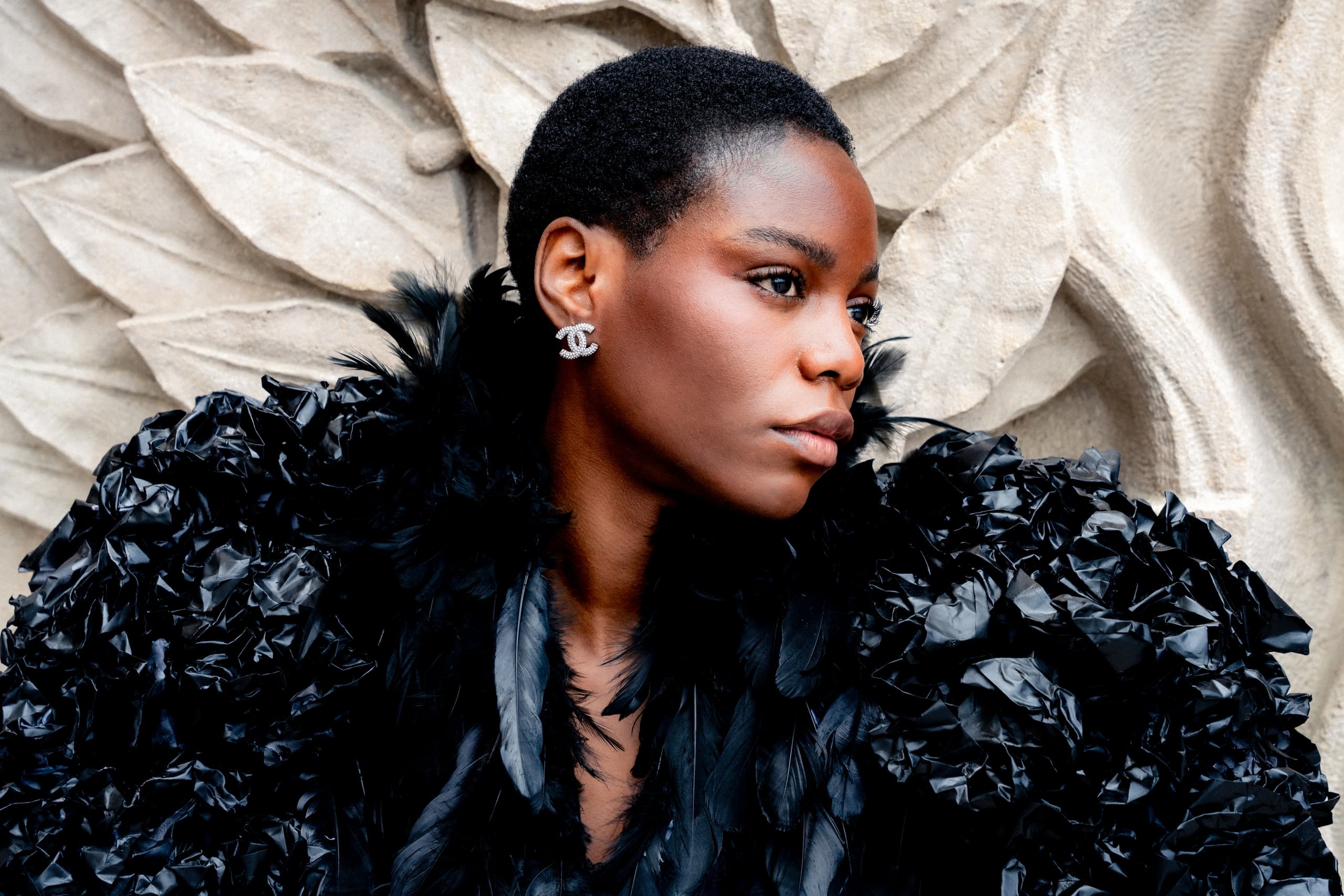 Stylish woman poses with black feathered outfit against textured background.