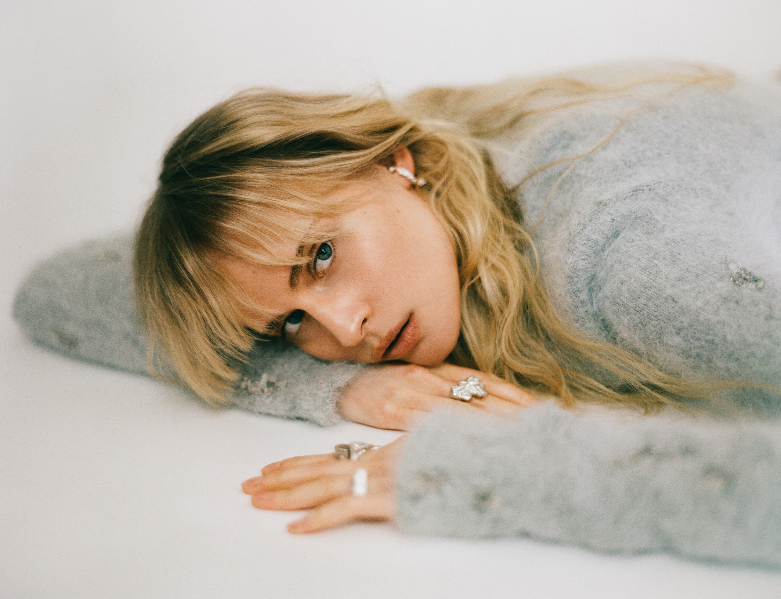 Woman in soft sweater lying down, wearing rings and looking thoughtful.