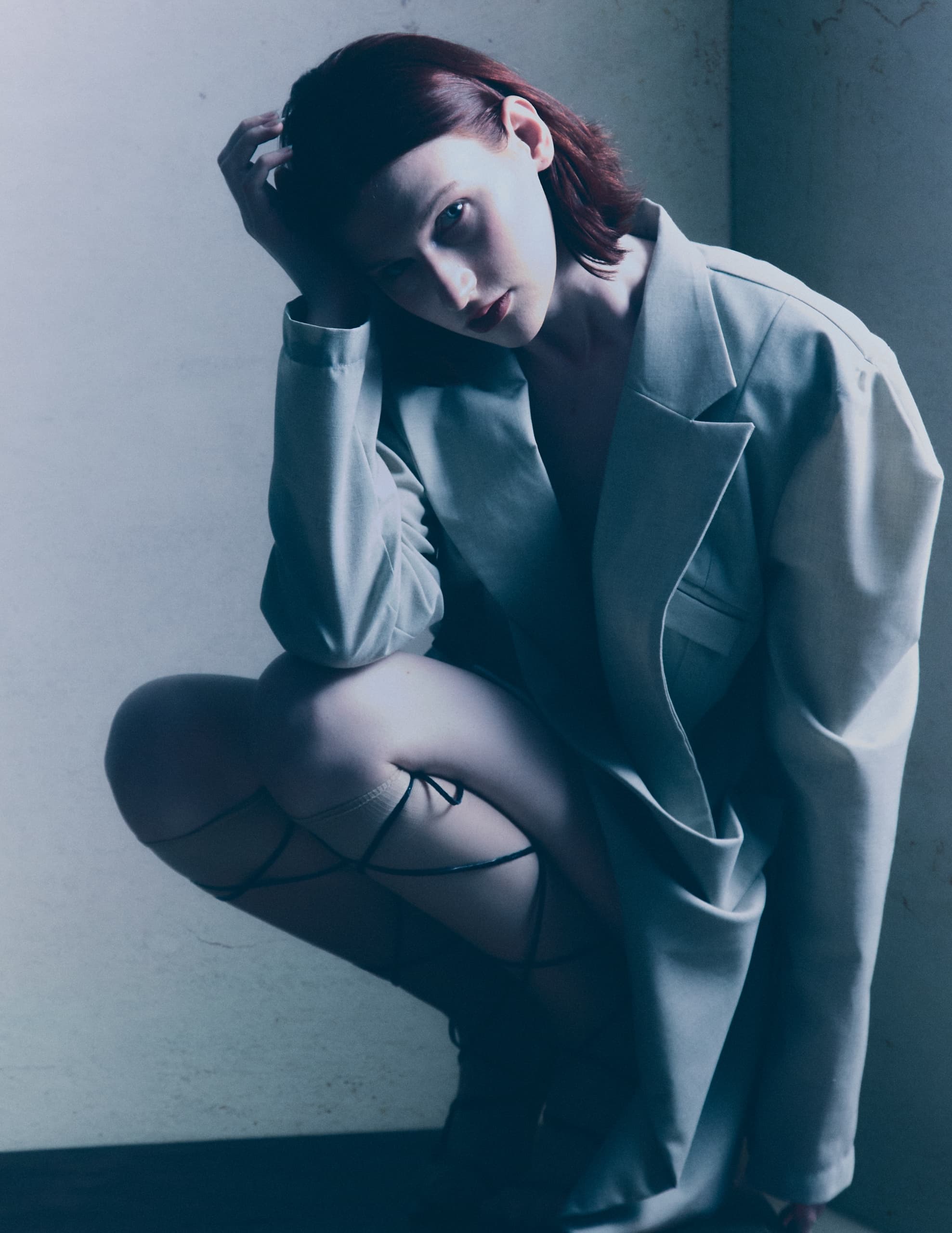Stylish woman in oversized blazer poses dramatically in low light.