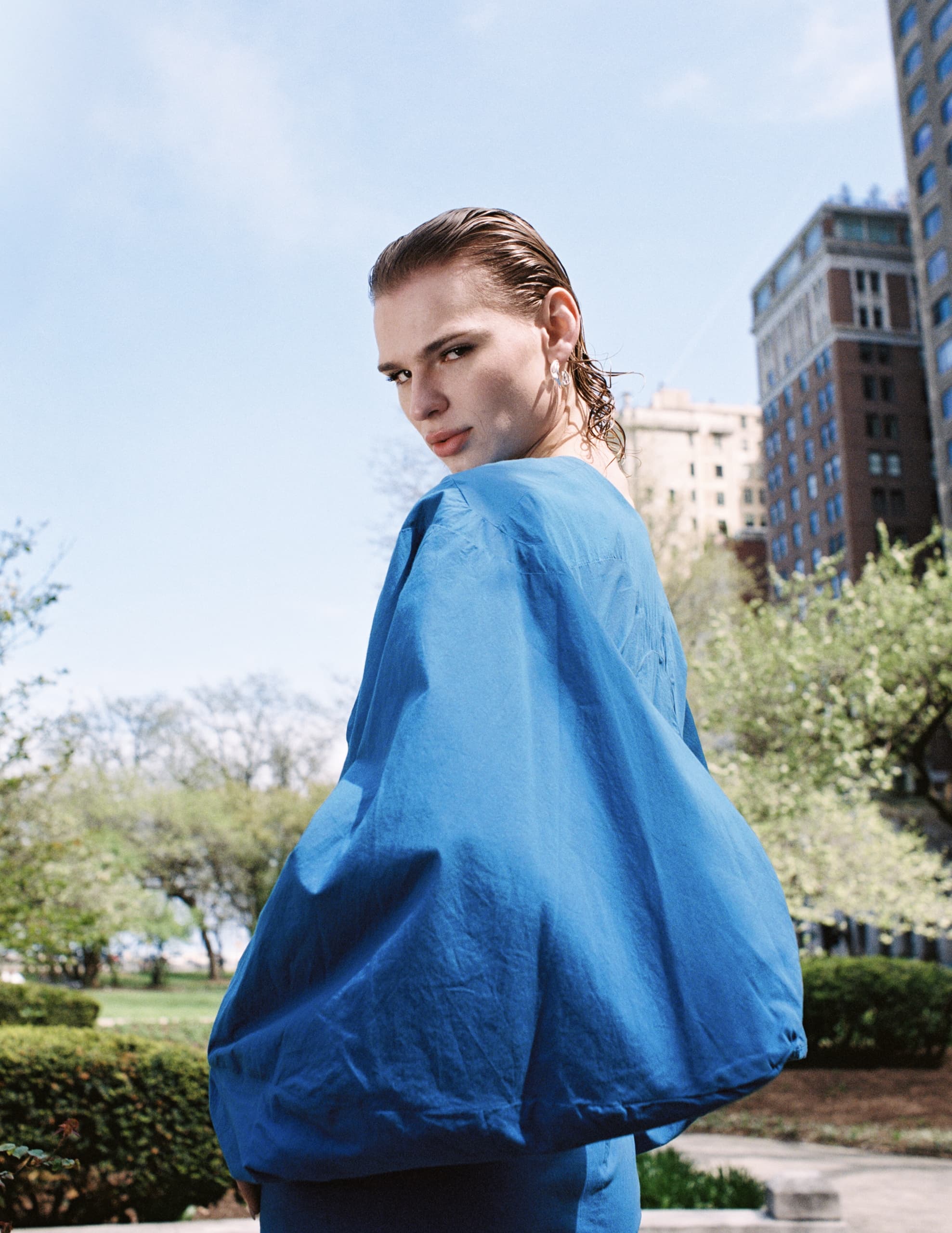 Person in blue jacket outdoors with trees and buildings in the background.