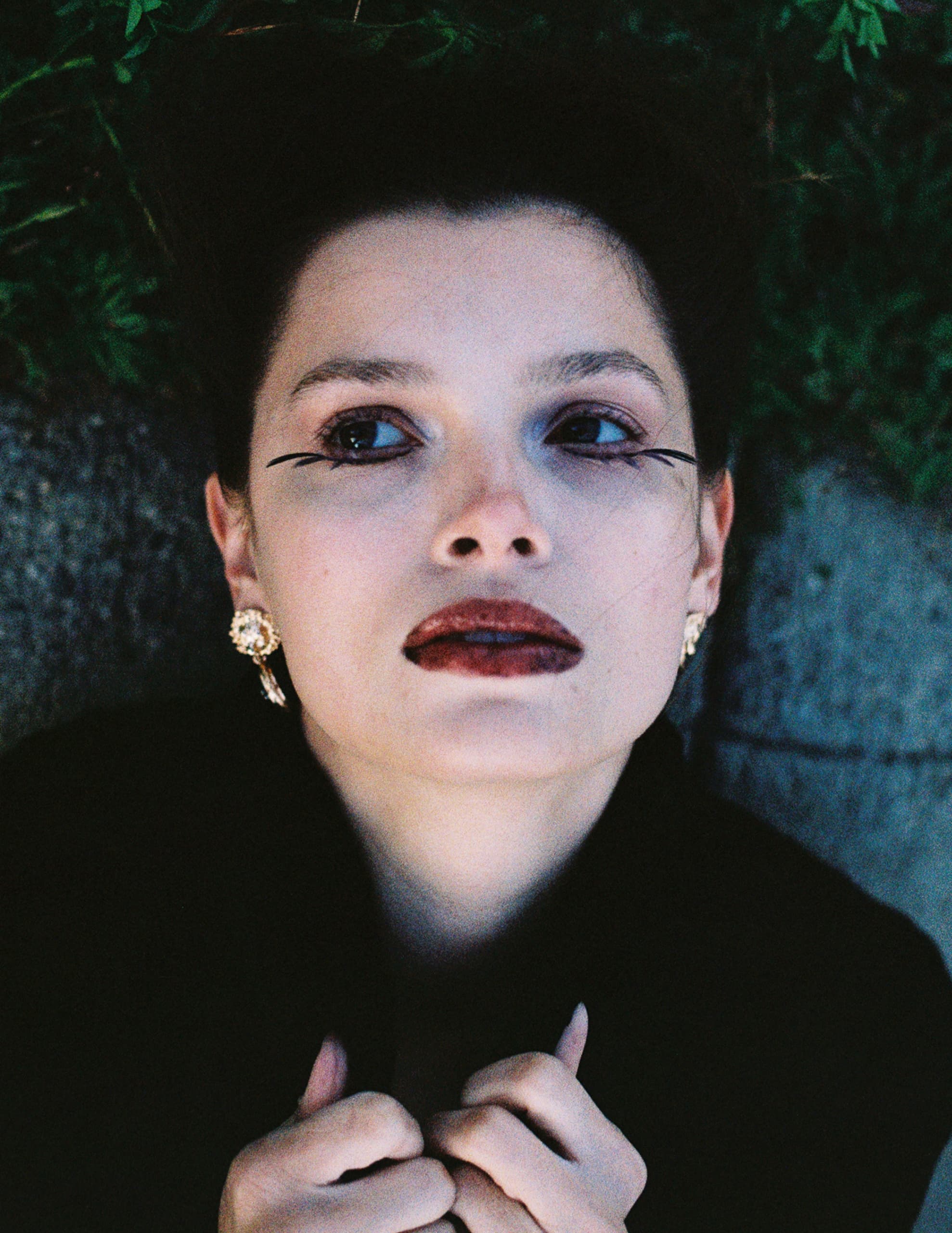 Woman with bold makeup and earrings, artistic portrait with dark lipstick and eyeliner.
