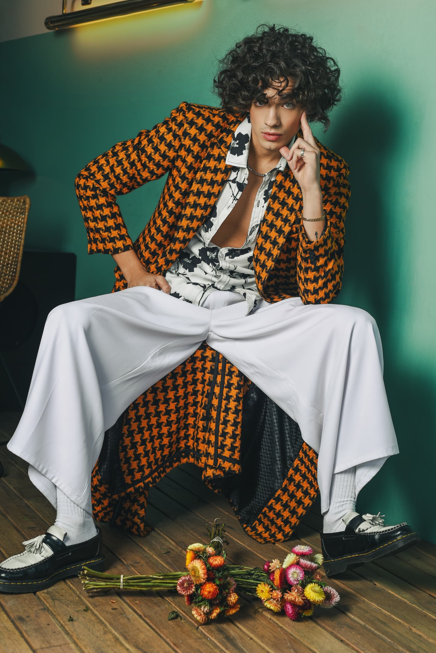 Fashionable person in retro outfit posing with flowers on wooden floor.