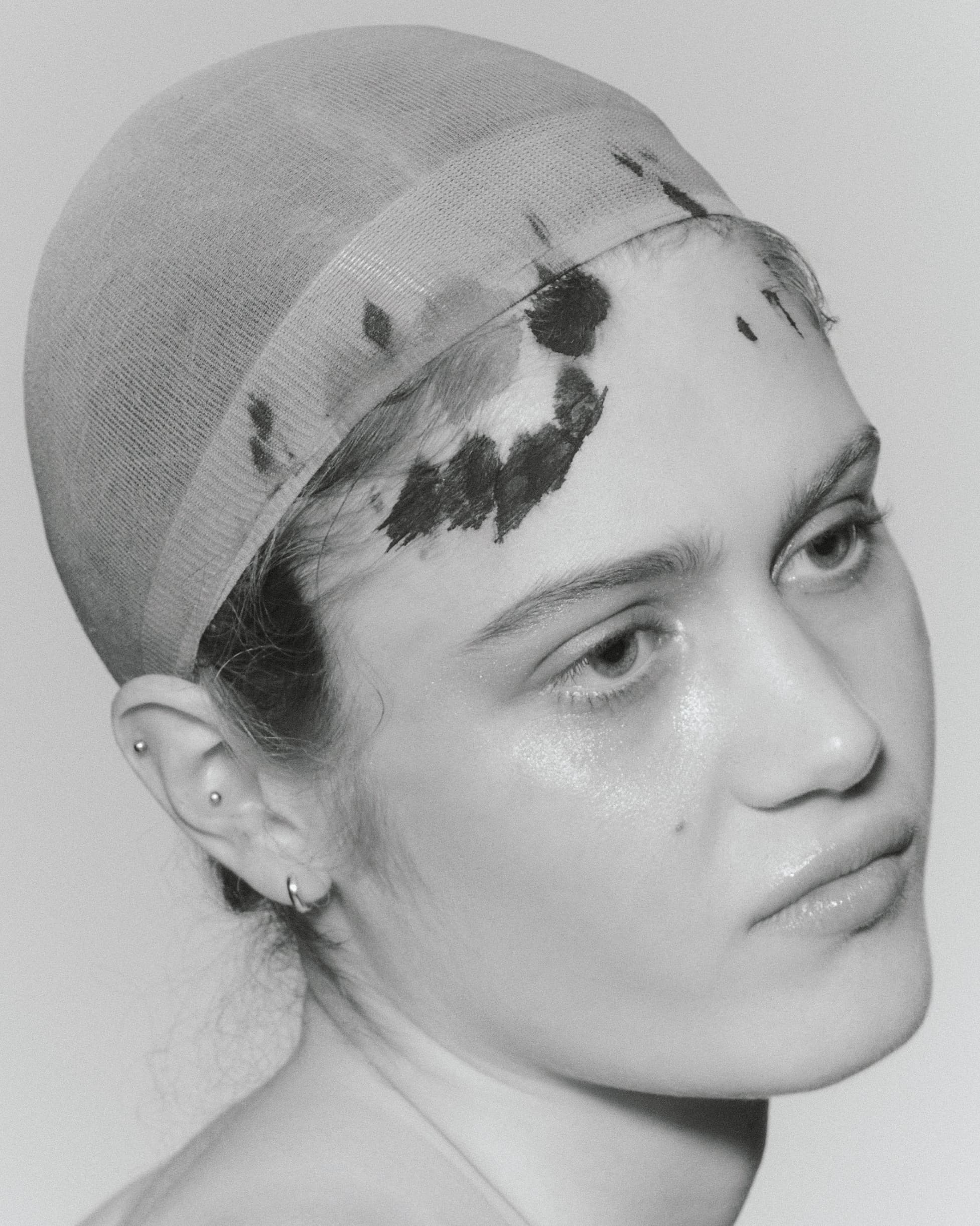 Black and white portrait of a person wearing a mesh cap with artistic paint detail.