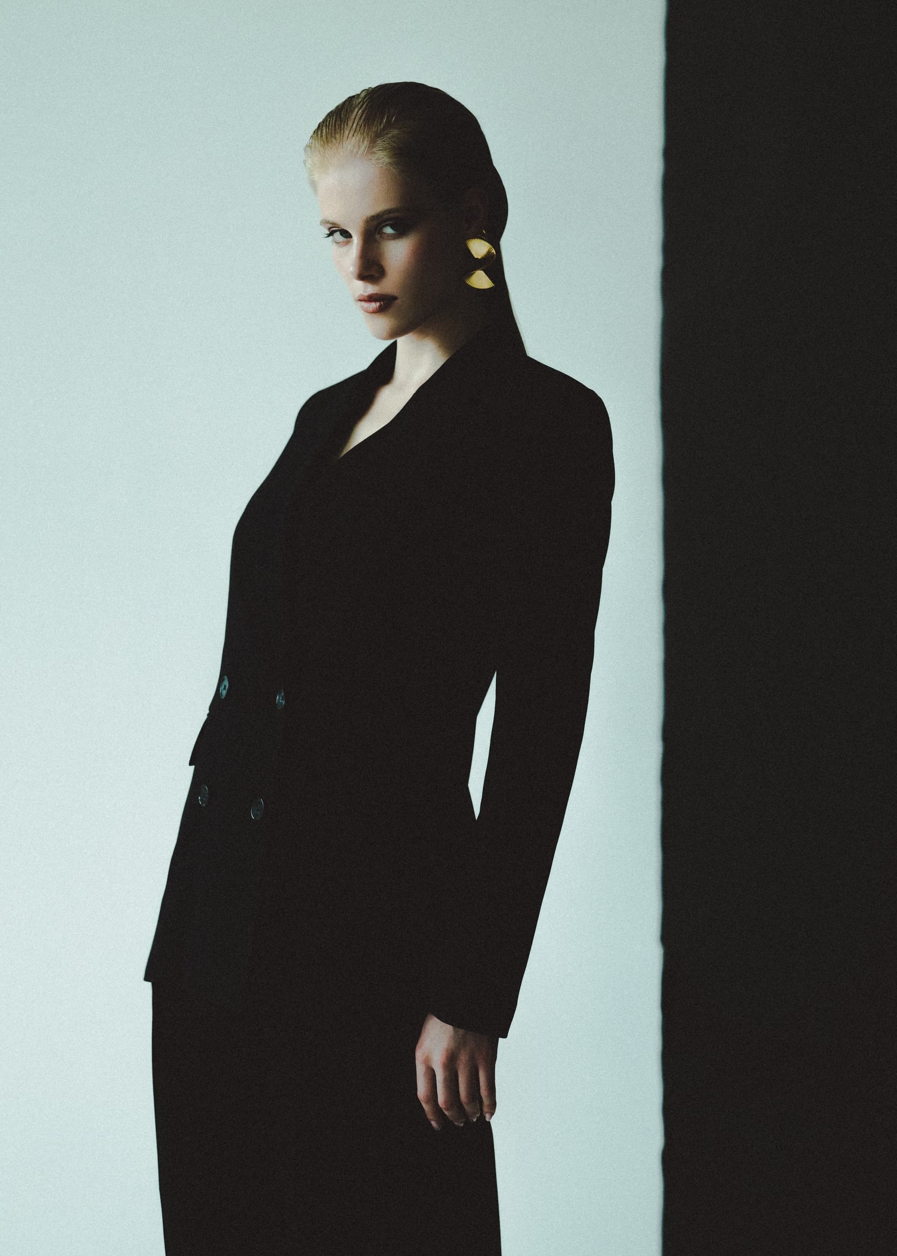 Elegant woman in a dark suit with bold earrings, striking a confident pose.
