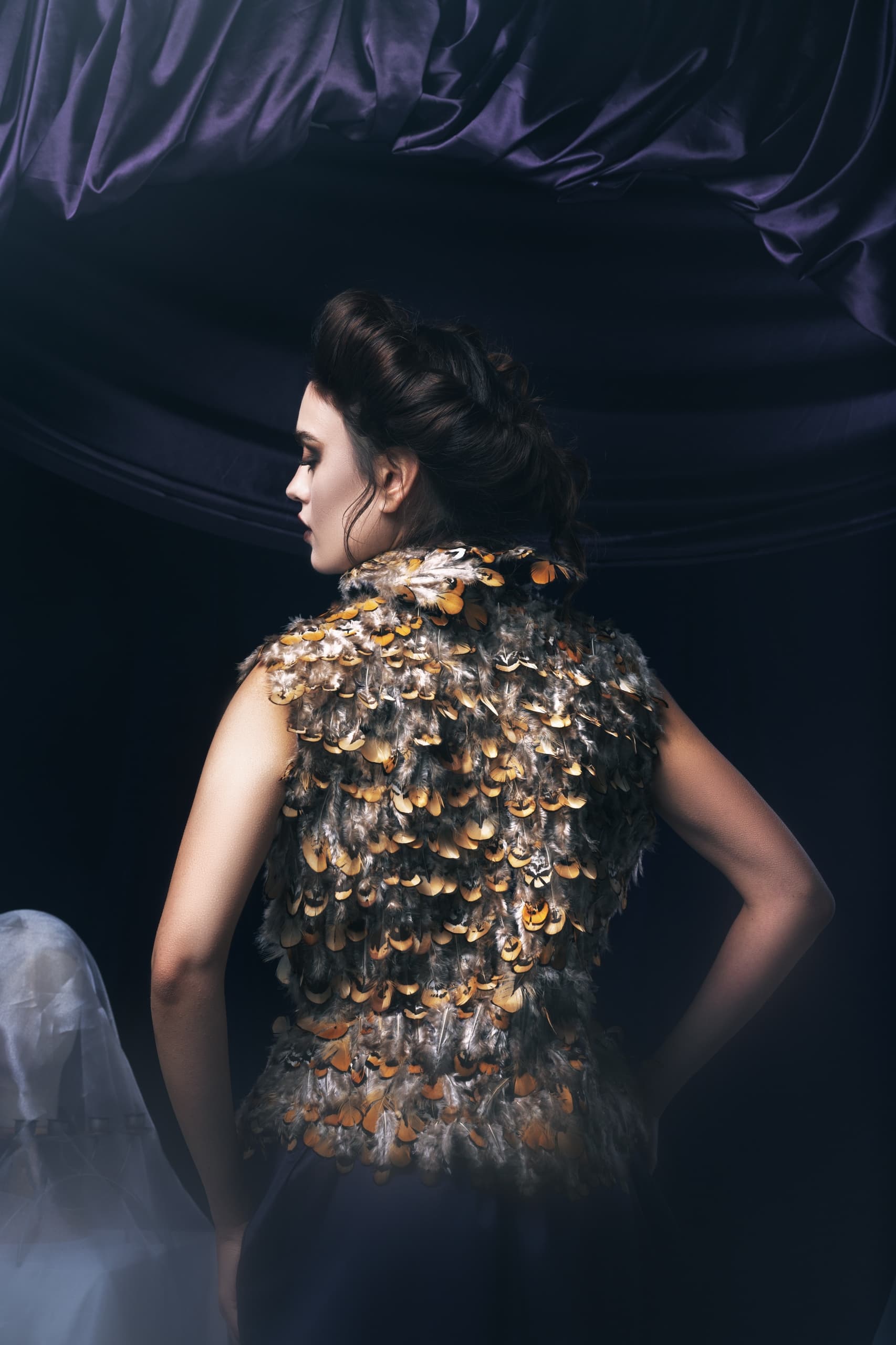 Woman in feathered fashion top, dark elegant background.