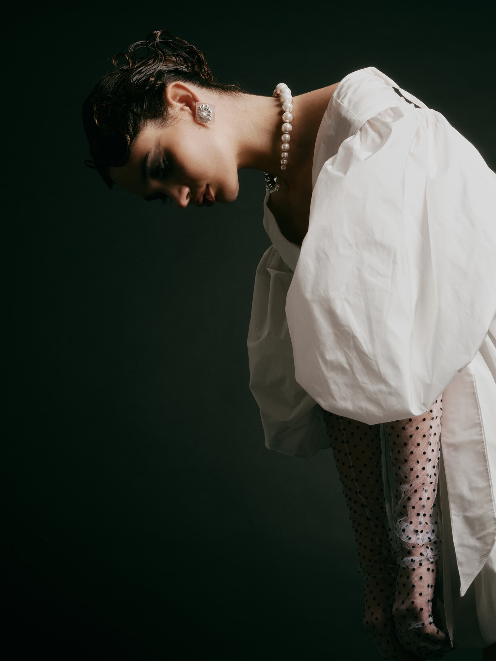 Fashion model in elegant white dress and pearls, striking a dramatic pose.