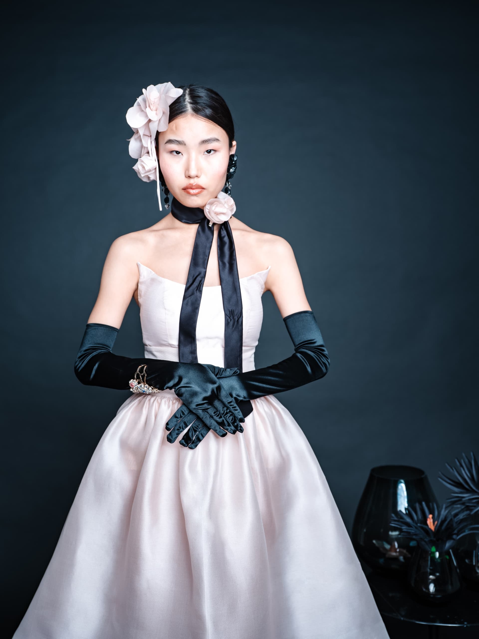 Elegant woman in vintage pink dress with floral headpiece and black gloves.
