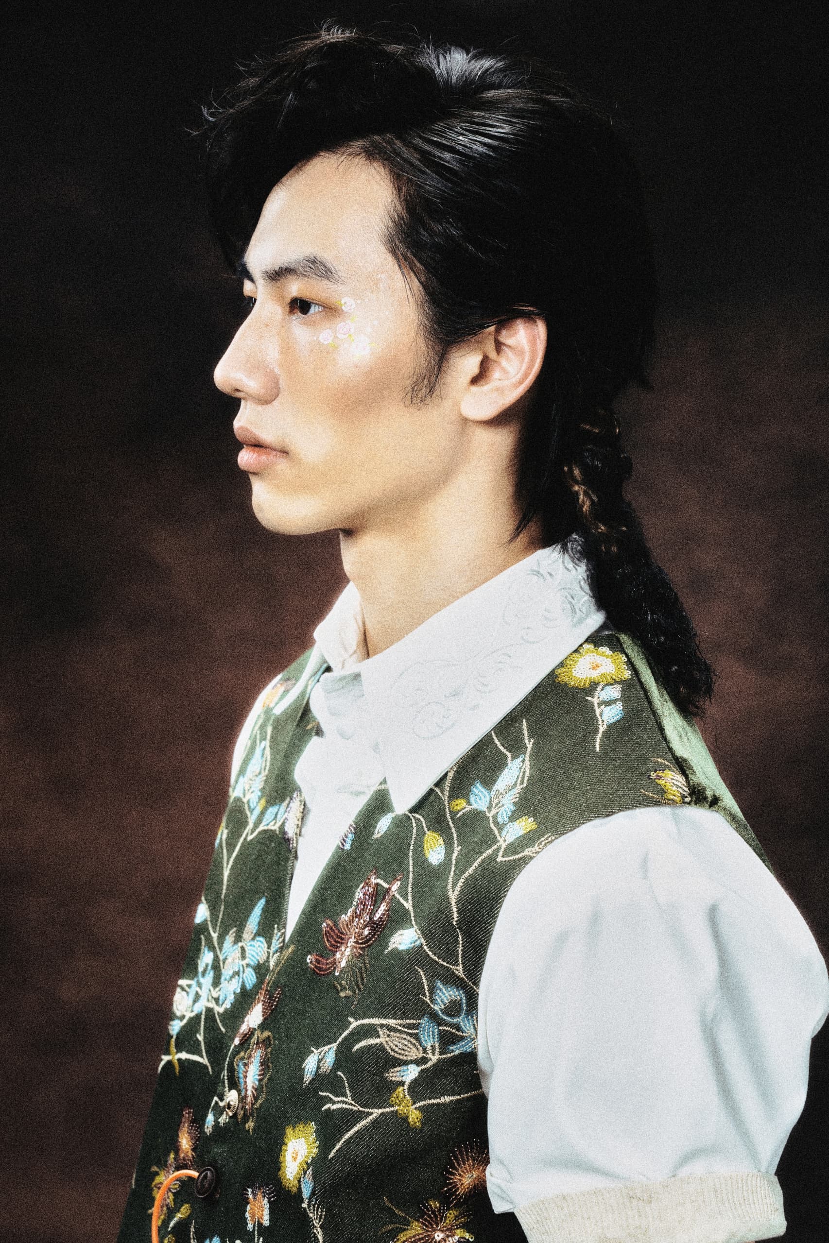 Model in embroidered vest with floral design, side profile view.