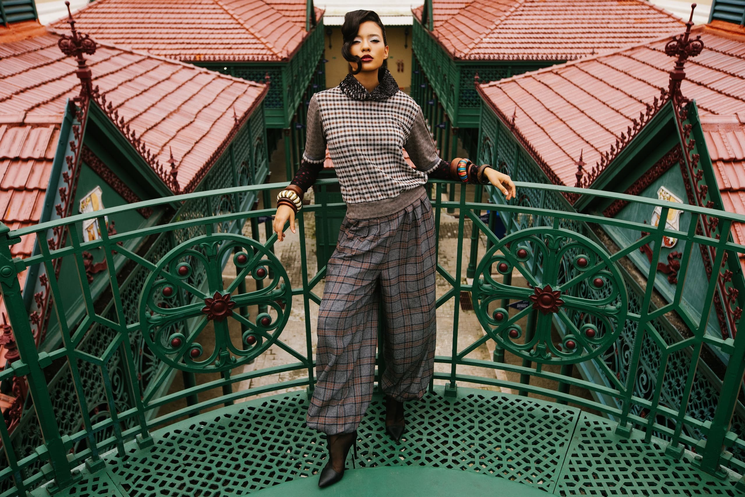 Fashionable person stands on ornate balcony with geometric architecture.