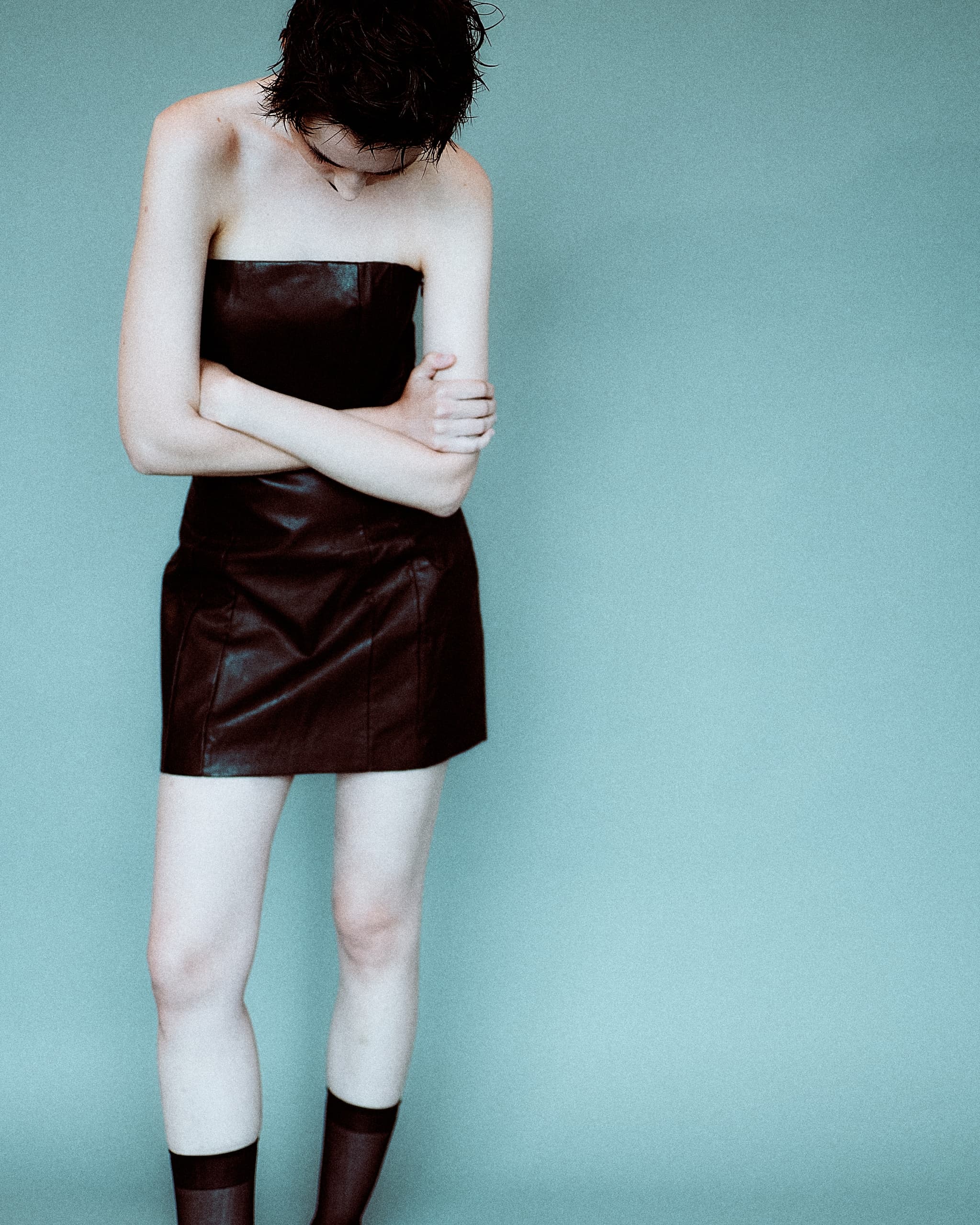 Person in strapless leather dress with crossed arms against blue background.
