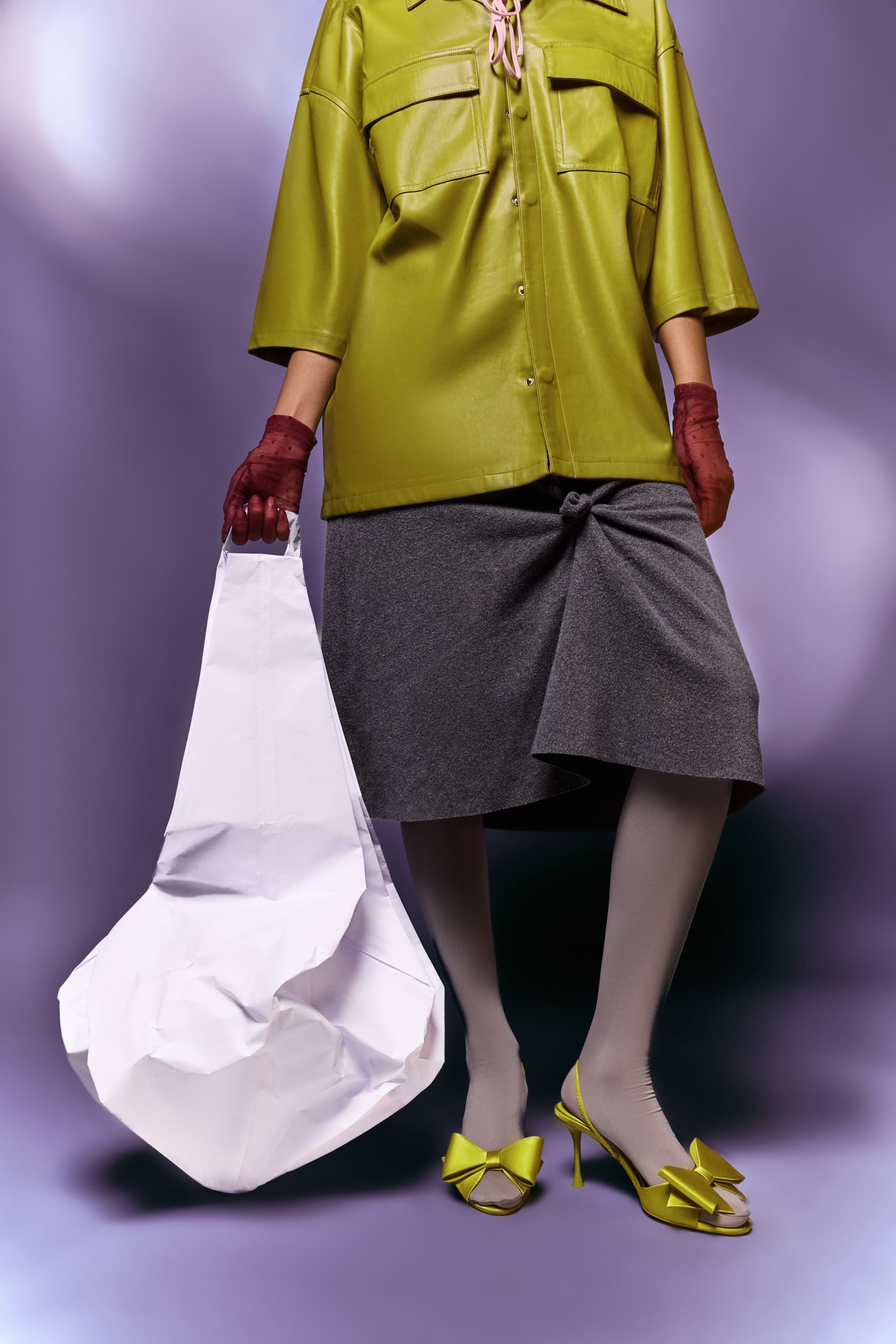 Stylish woman in green outfit with gray skirt and bold accessory bag.