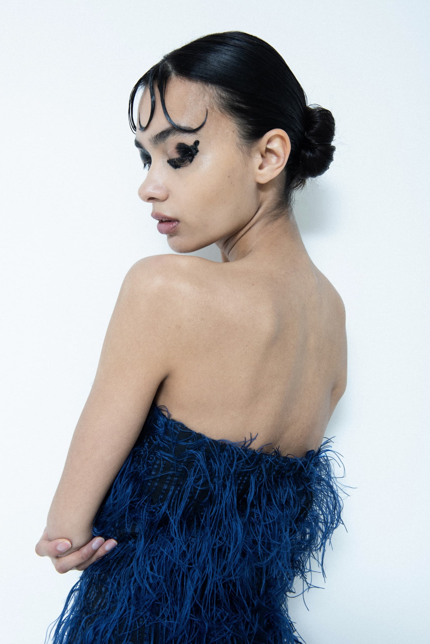 Elegant woman in blue feathered dress, side view pose against white background.