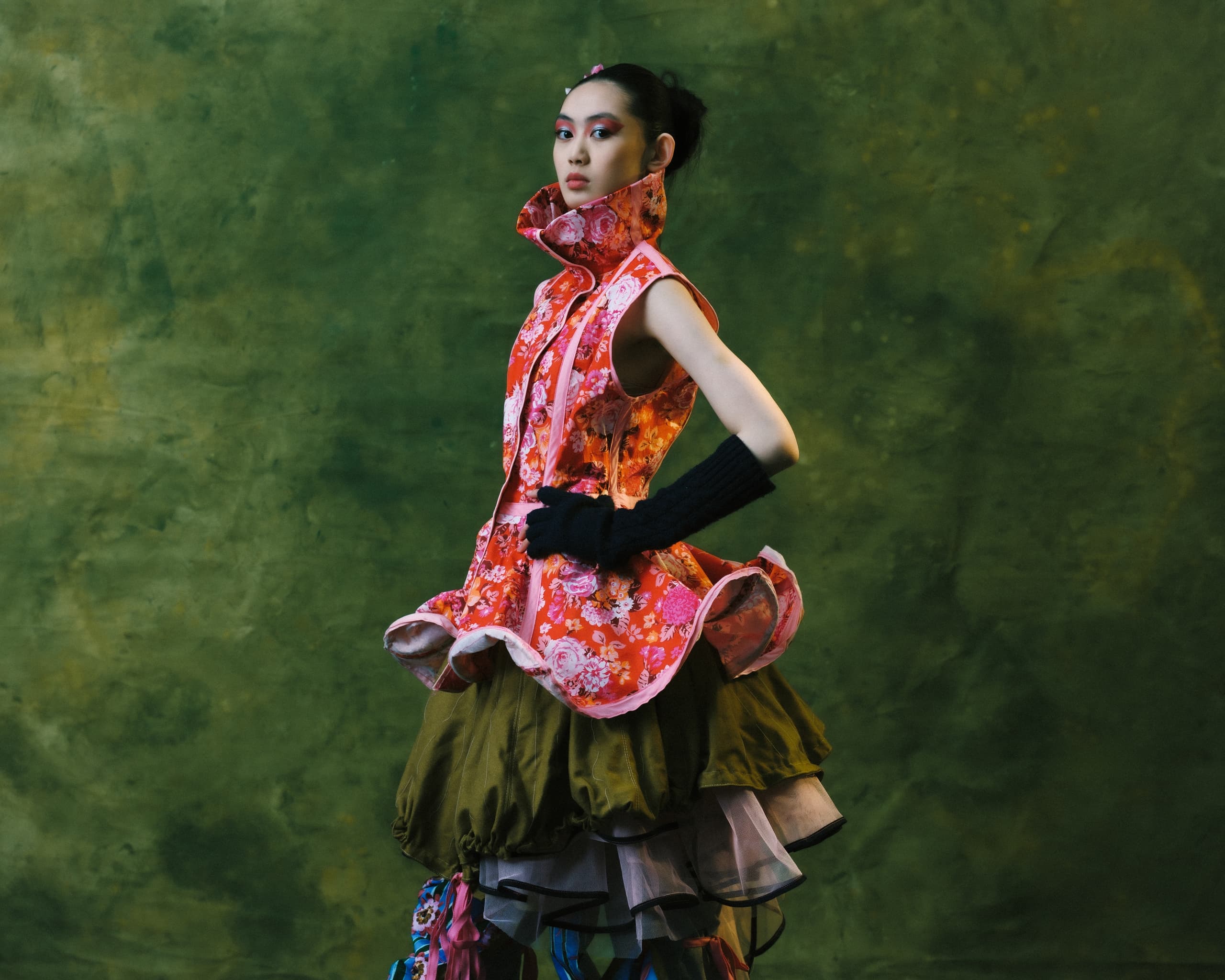 Fashion model in colorful, layered dress against a green background.