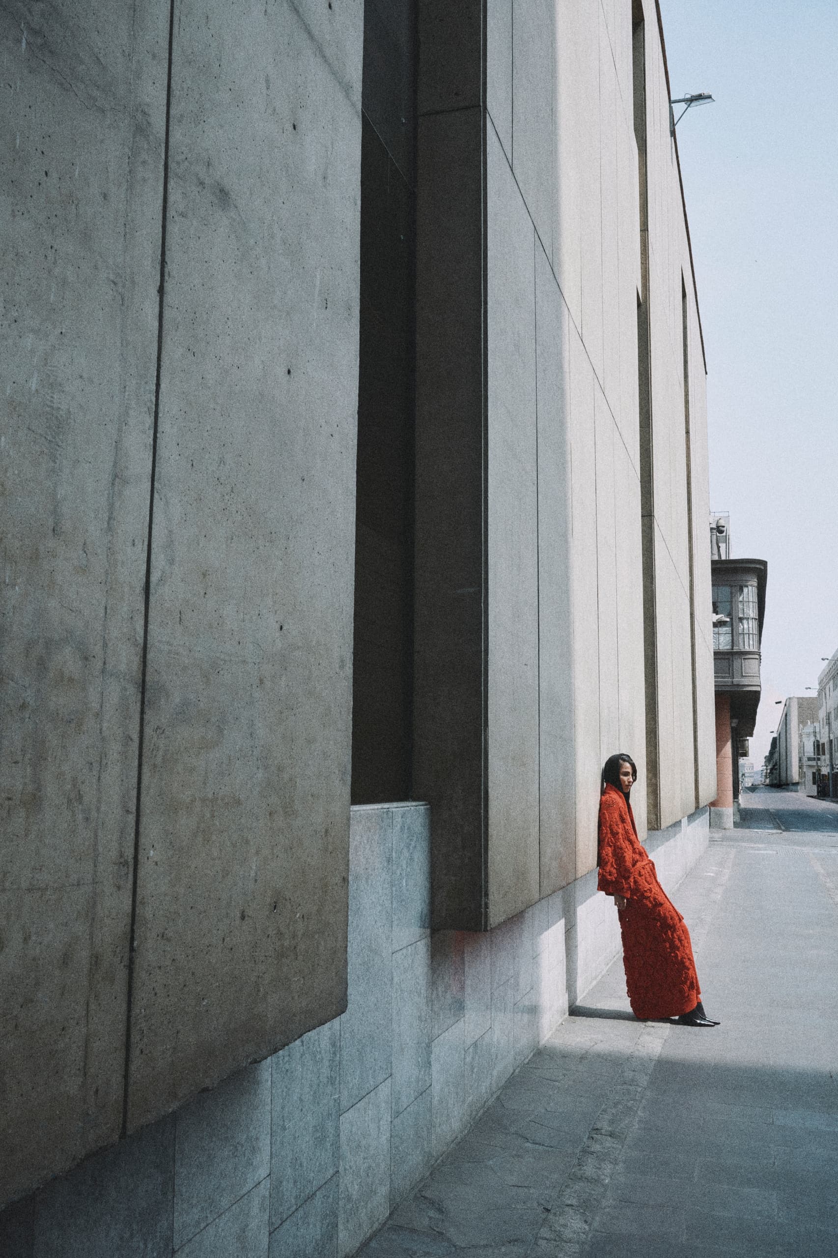 Person in red dress leans against urban wall on a sunny day