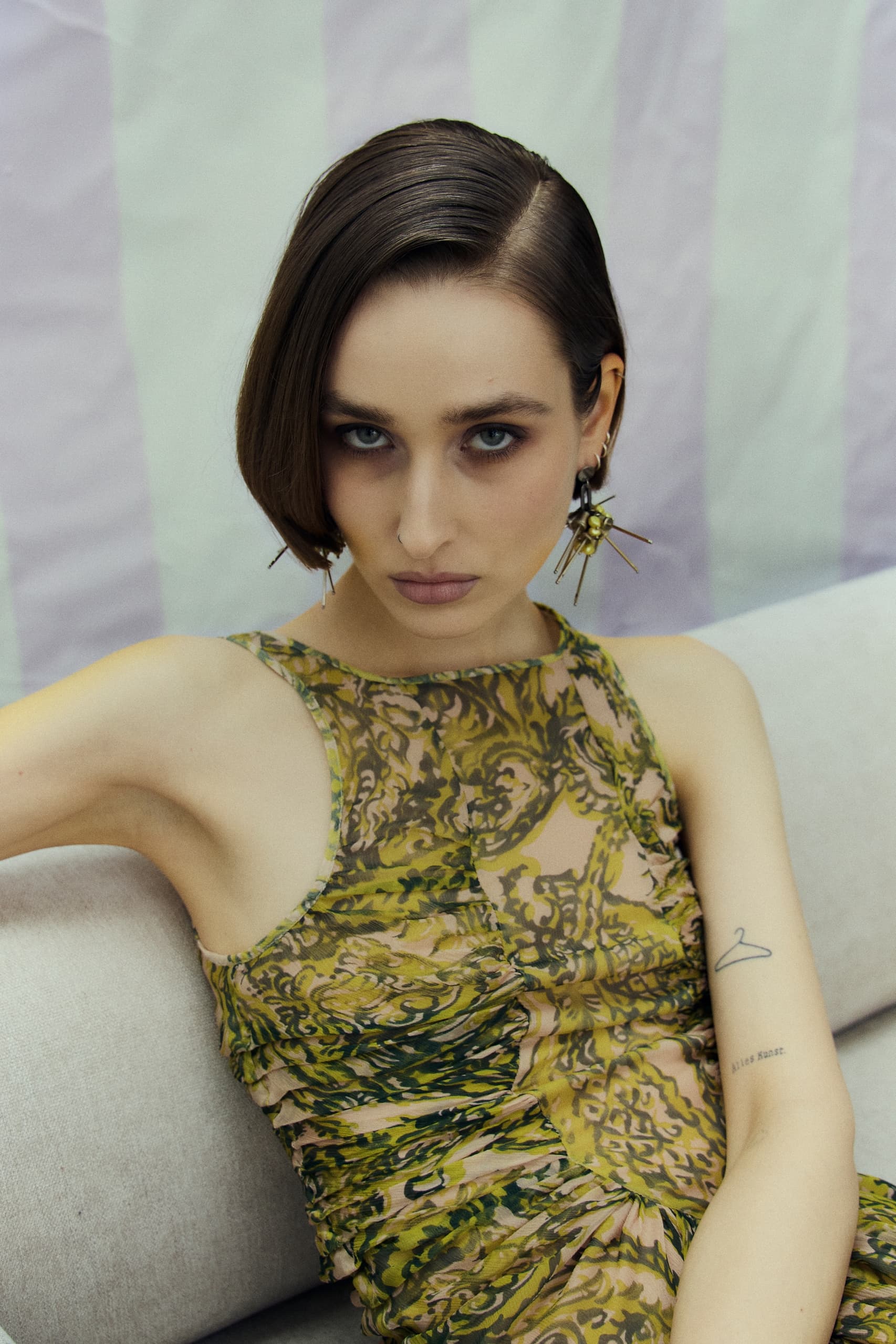 Fashionable woman in a patterned dress with edgy earrings, posing elegantly on a sofa.