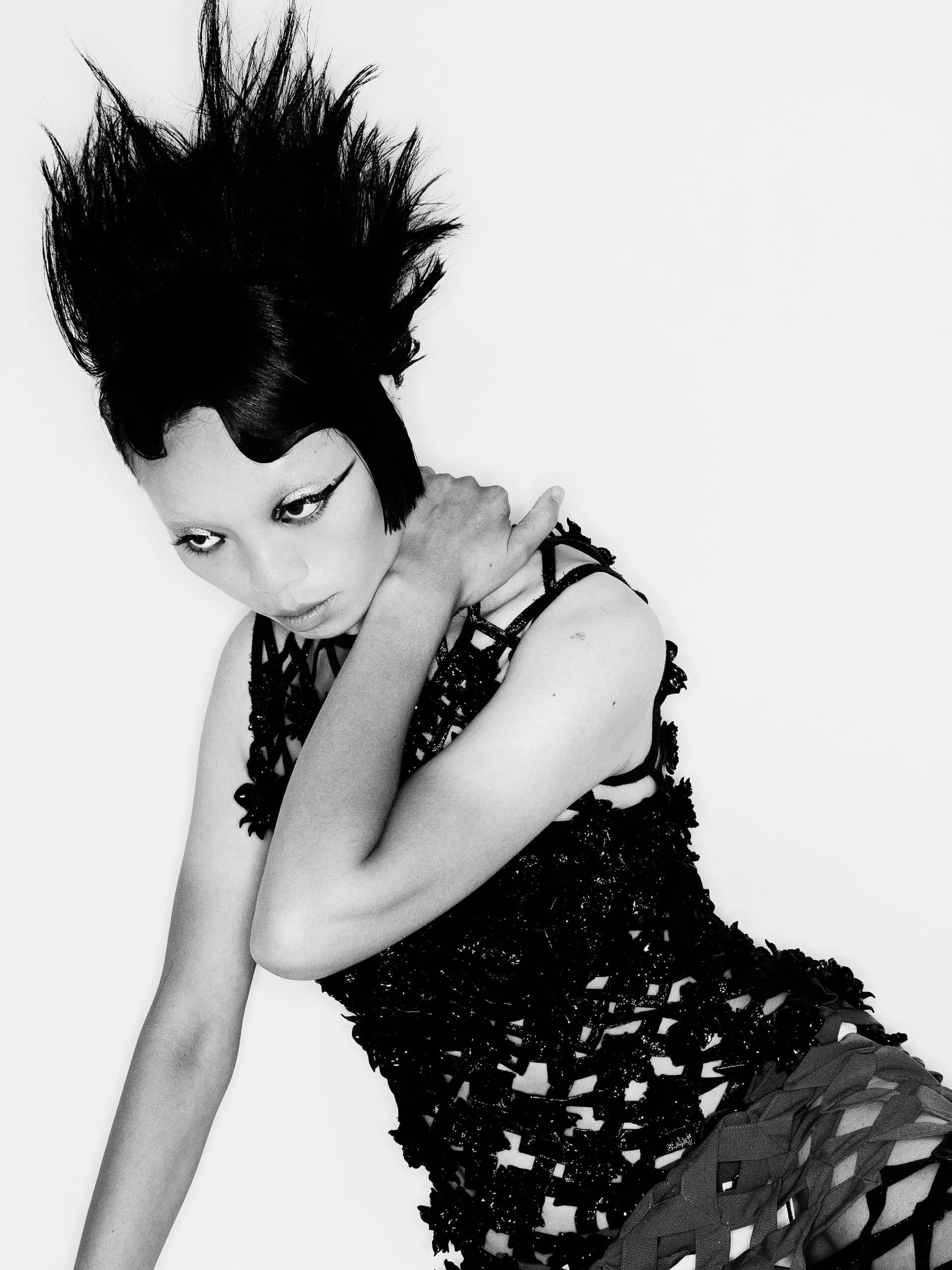 Fashion model with edgy hairstyle and striking makeup in black woven attire.