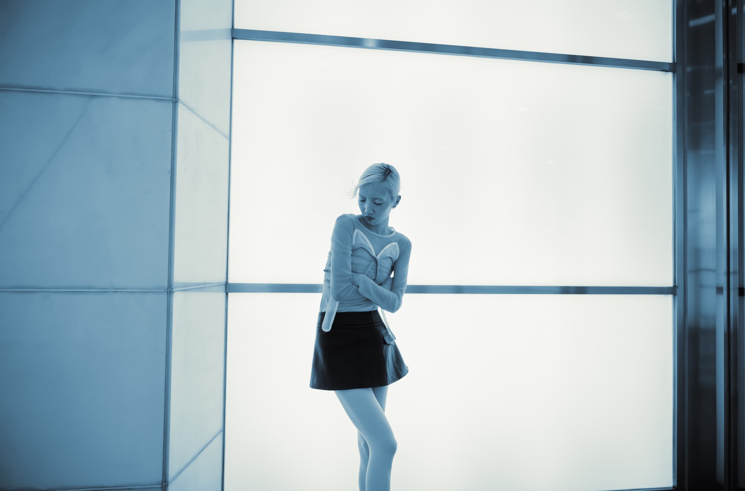 Woman in stylish attire poses against a modern, minimalist light wall backdrop.