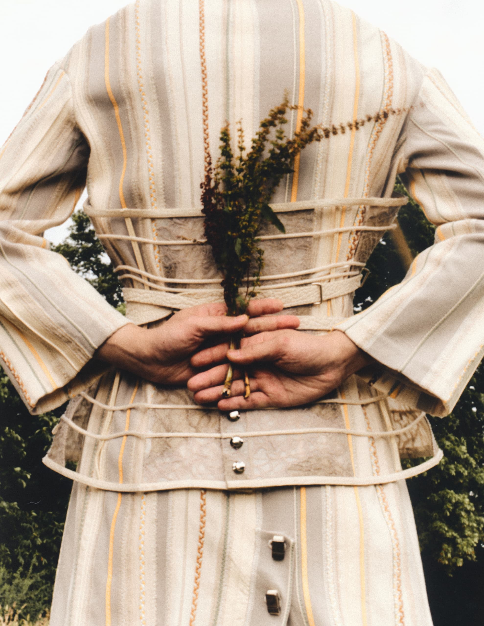 Person holding flowers behind back in striped vintage outfit.