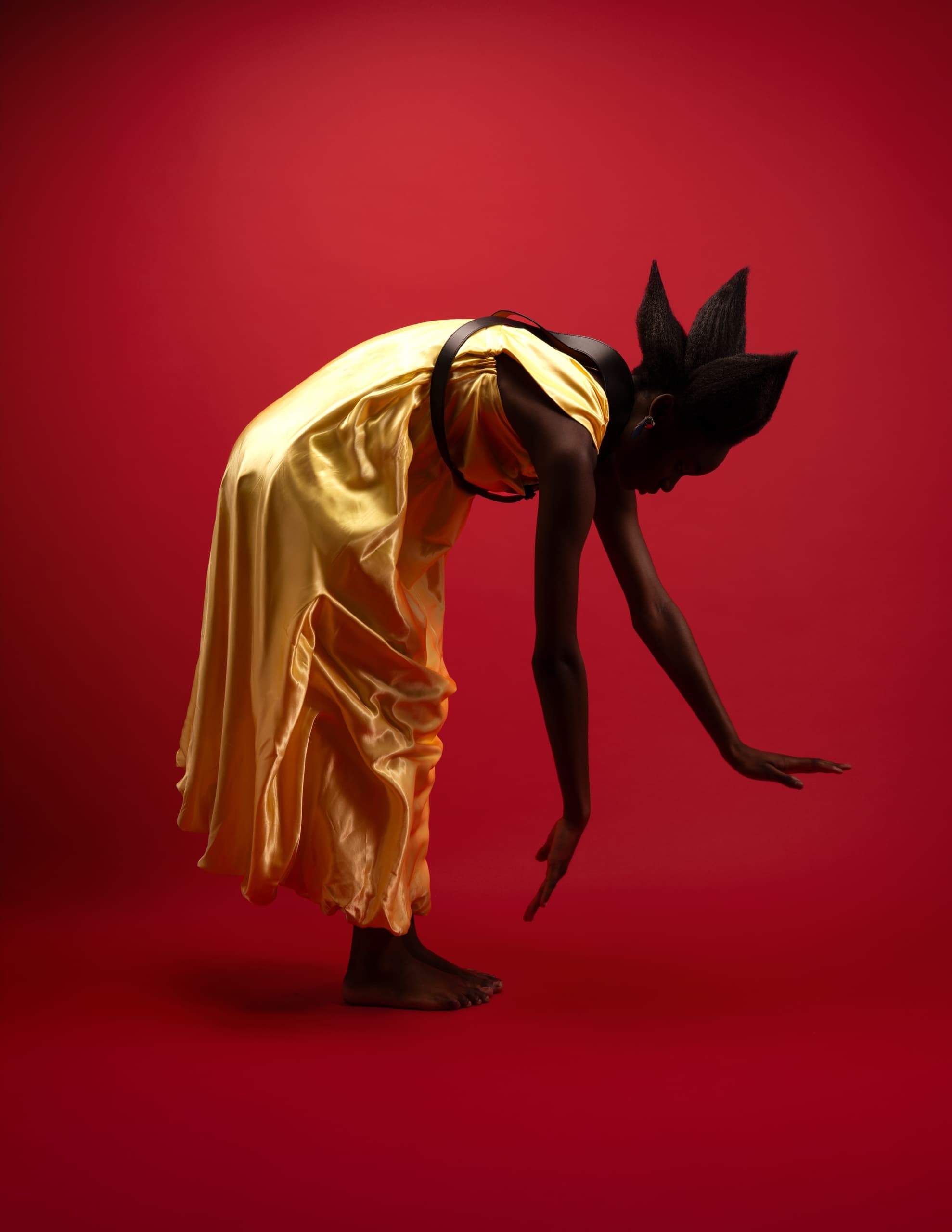 Person in gold gown posing against a vibrant red background, modern artistic expression.