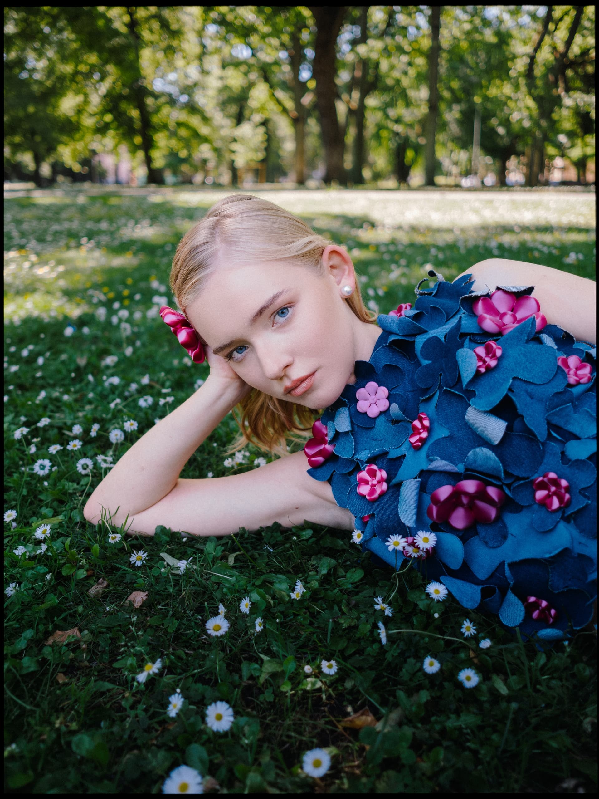 Woman in floral dress lying on grass in sunny park.
