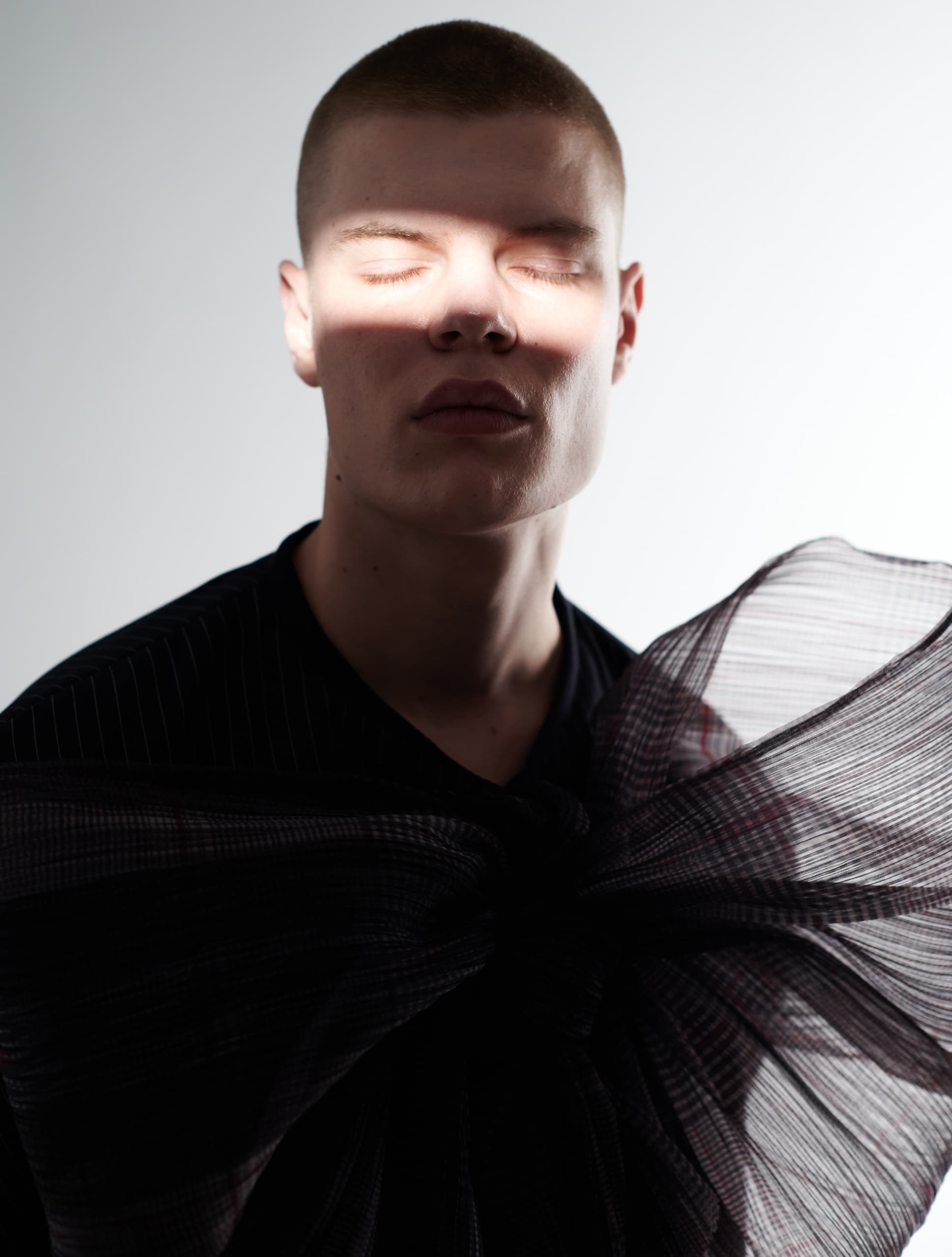 Person with closed eyes, sunlight on face, wearing sheer plaid fabric.