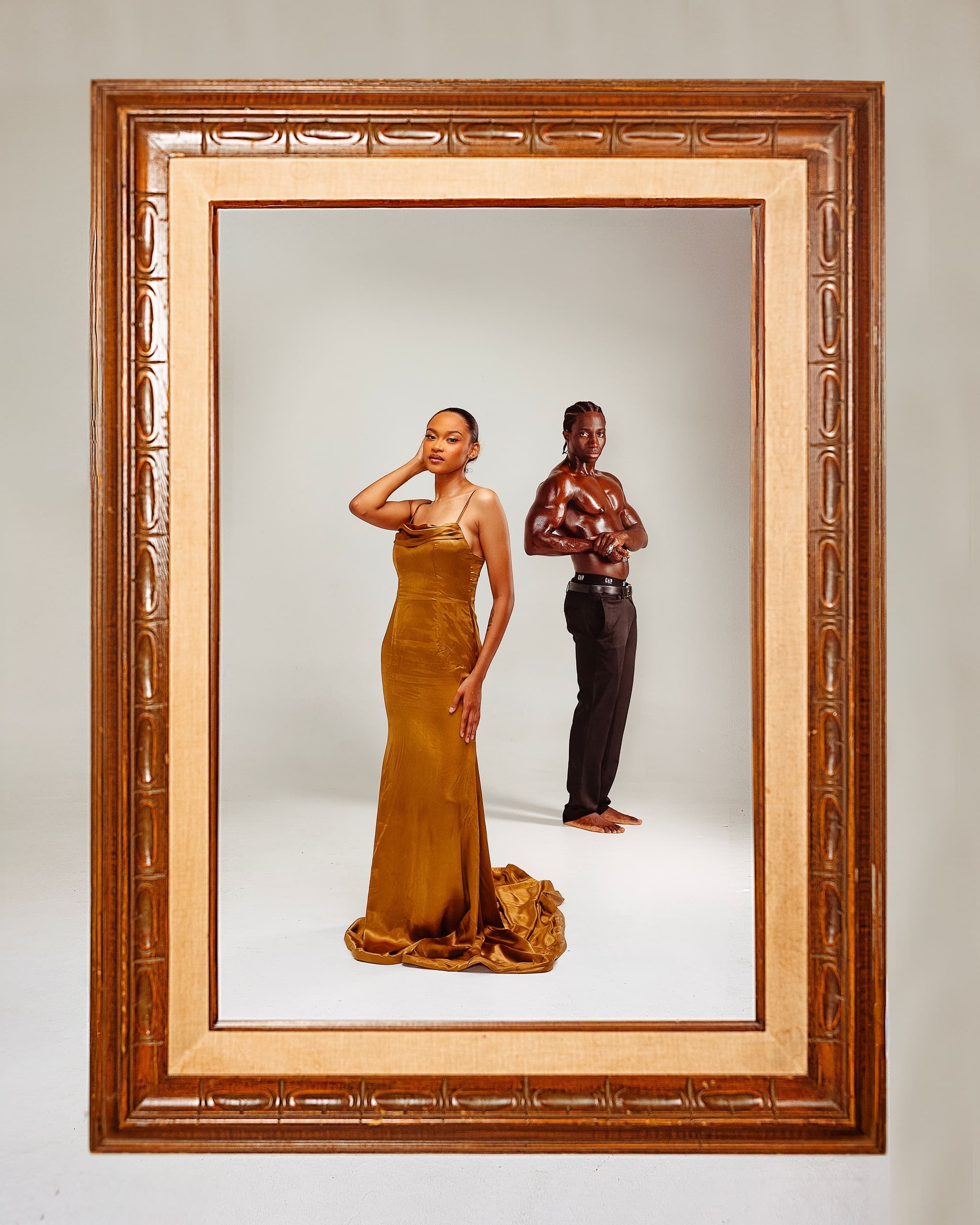 Elegant framed portrait of a woman in a gold dress and a shirtless man striking a pose.