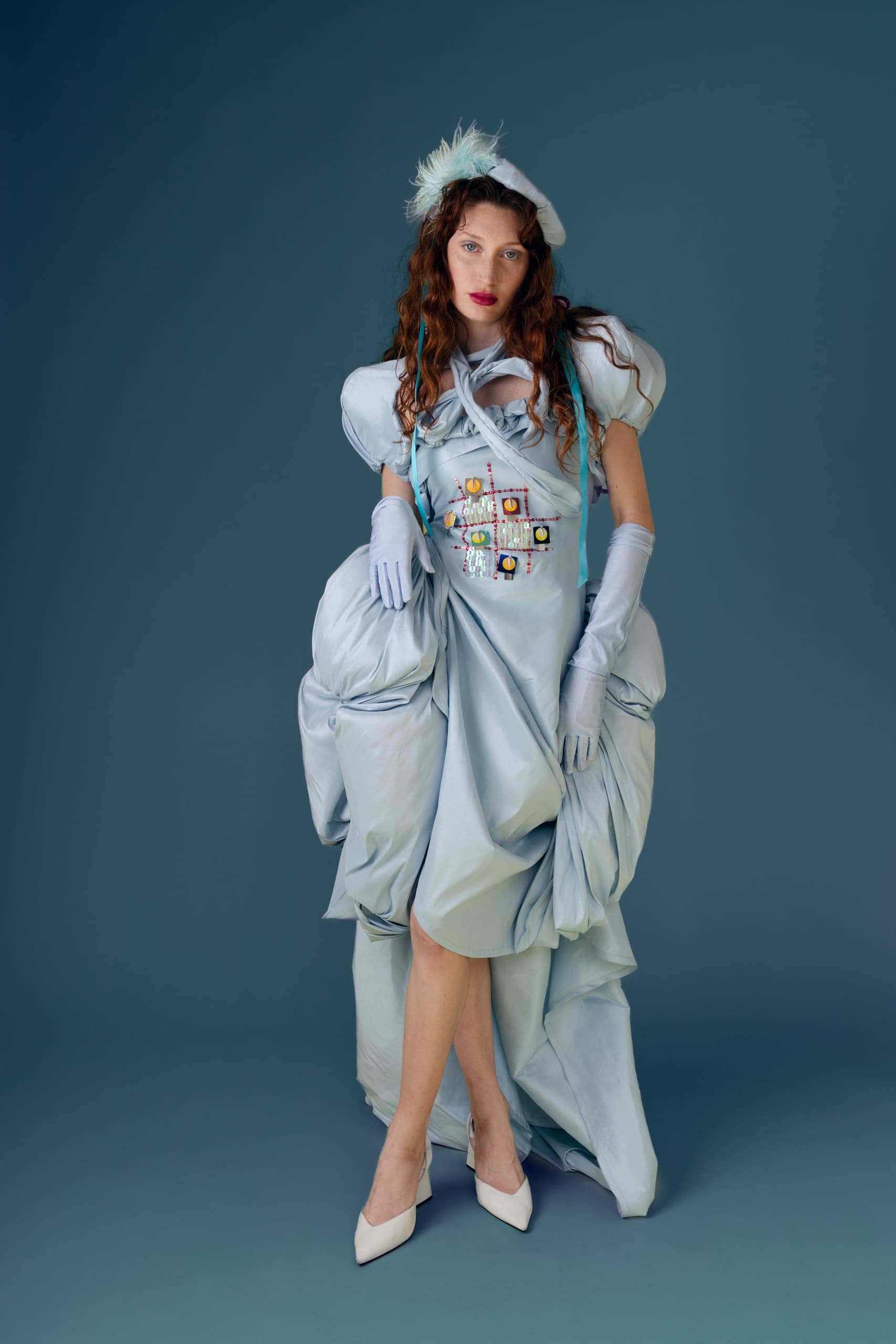 Elegant woman in a blue, structured gown posing against a blue background.