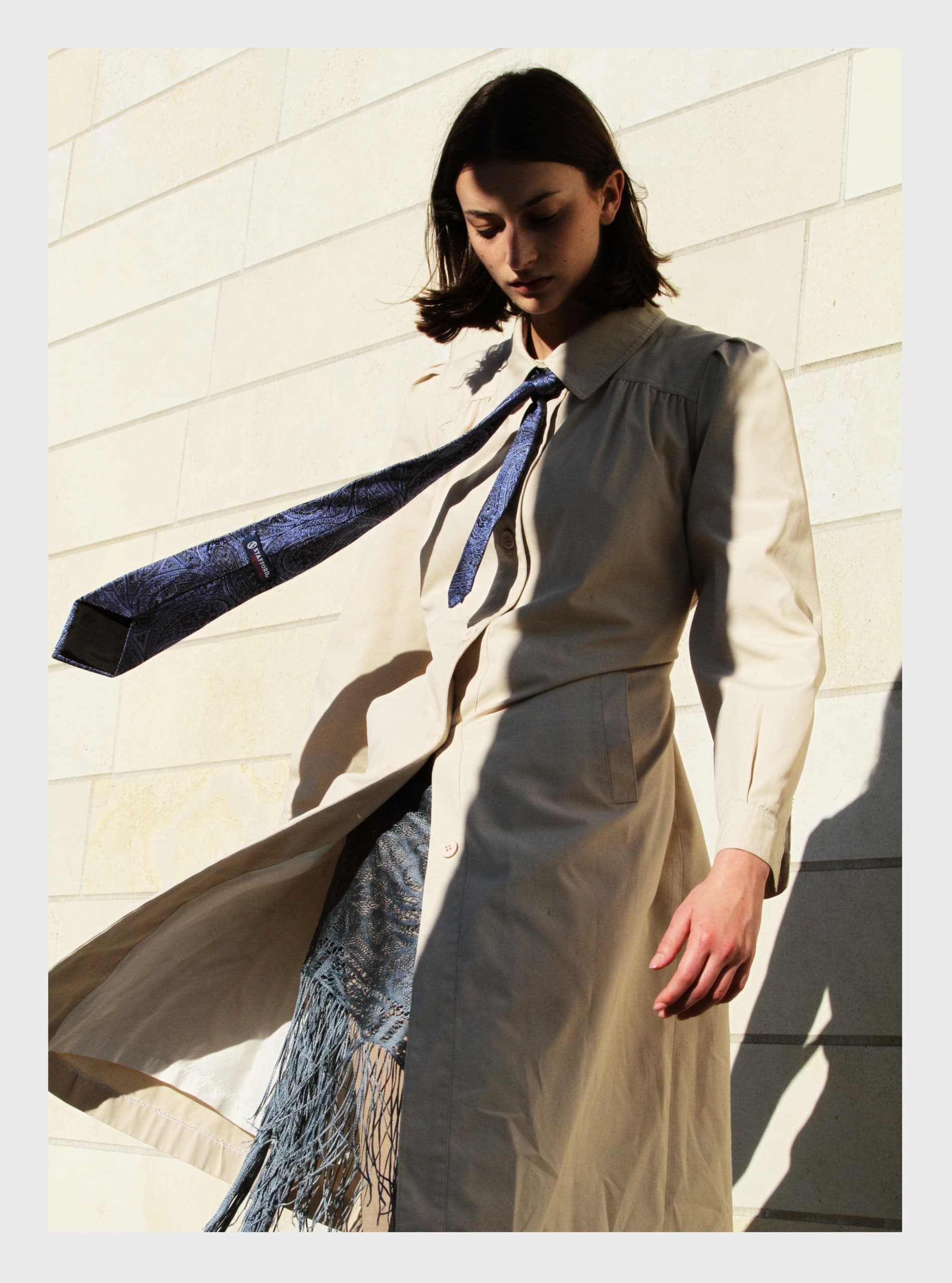 Fashionable woman in a beige coat with blue tie flowing in sunlight.