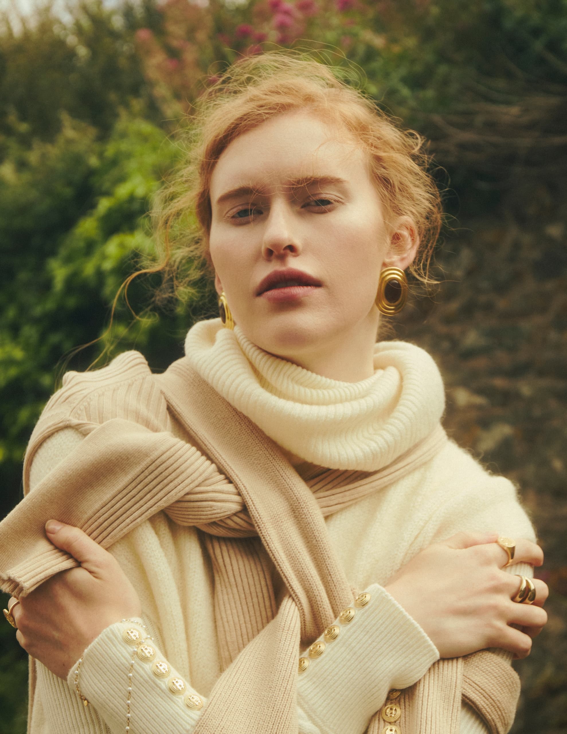 Young woman in cozy knit sweater and scarf, with gold accessories, outdoors.