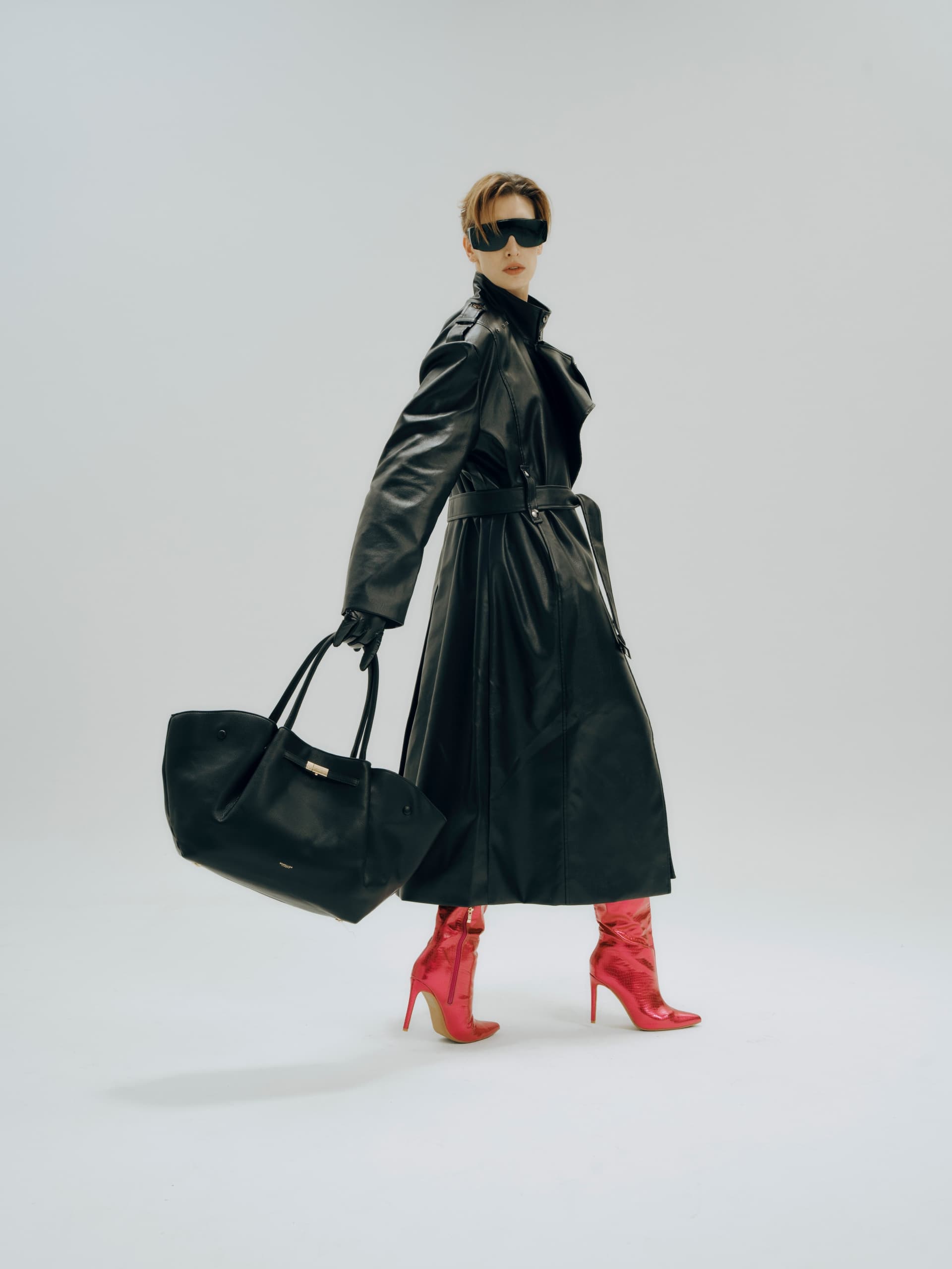 Fashionable woman in black coat, red boots, sunglasses, and bag on white background.