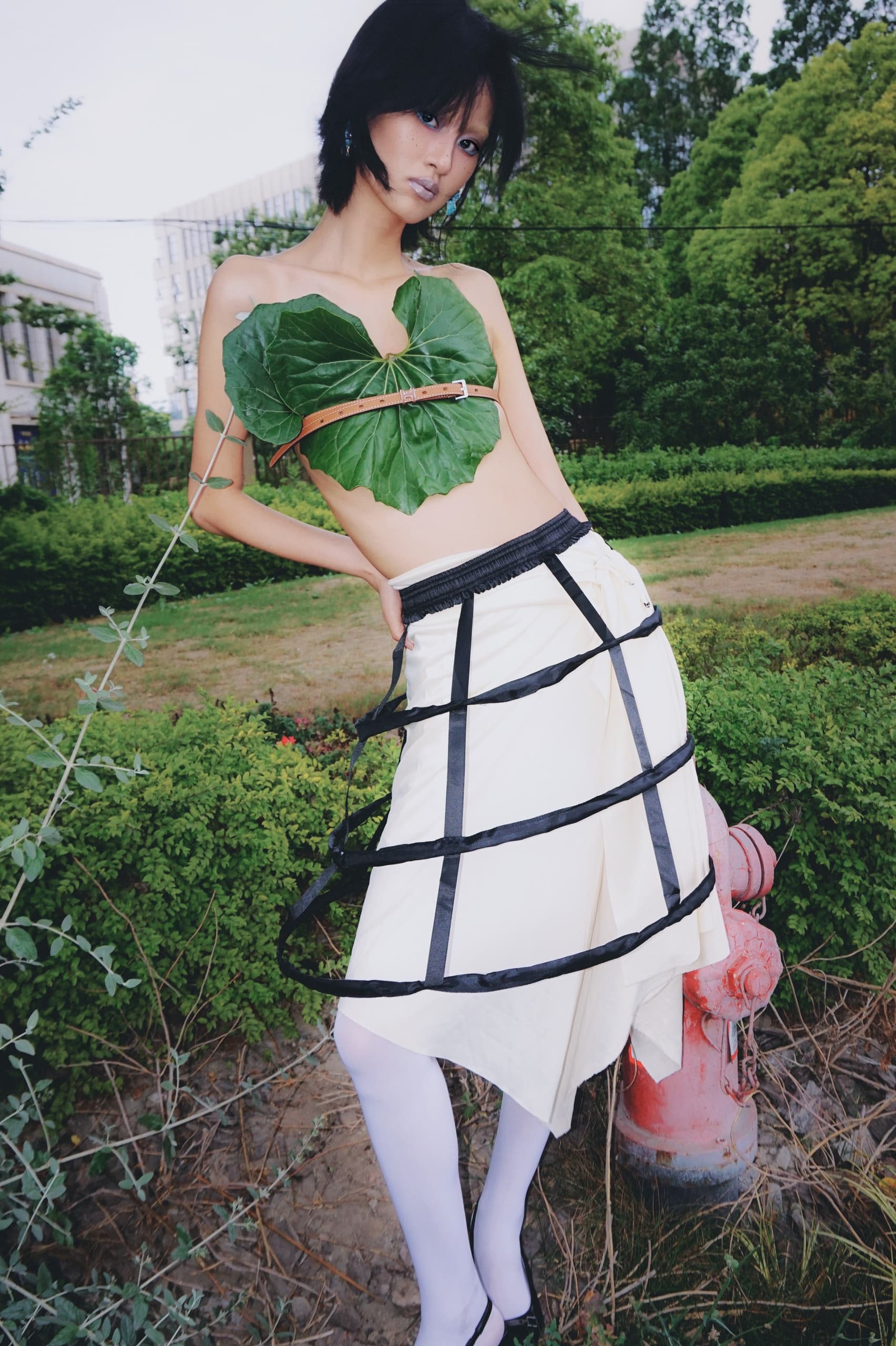 Fashion model in nature-inspired outfit beside greenery.