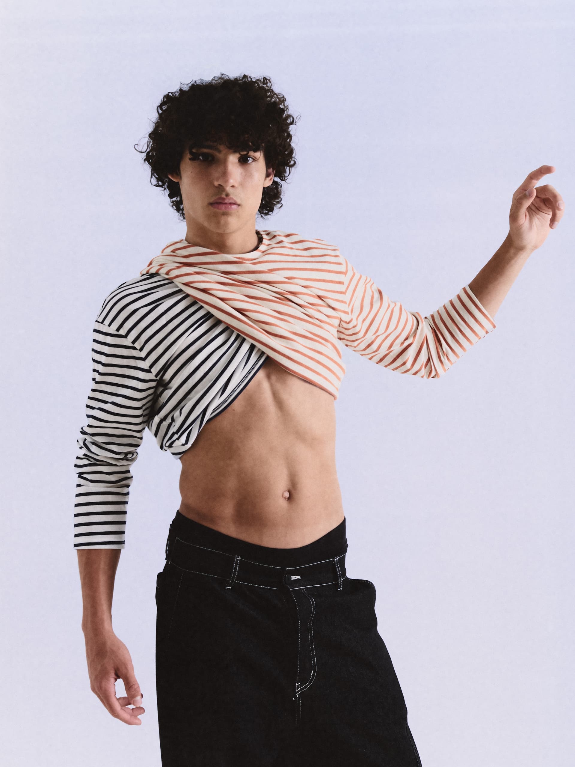 Fashionable model in a unique striped top poses stylishly against a plain background.
