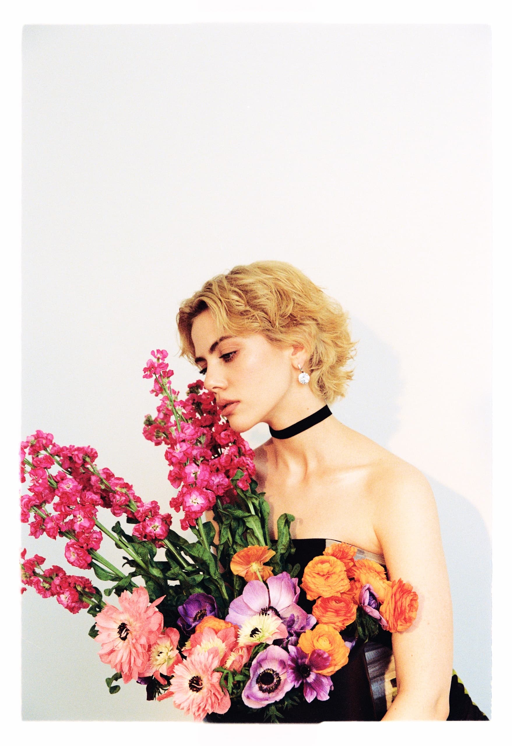 Person holding vibrant bouquet against a light background, wearing a black choker.