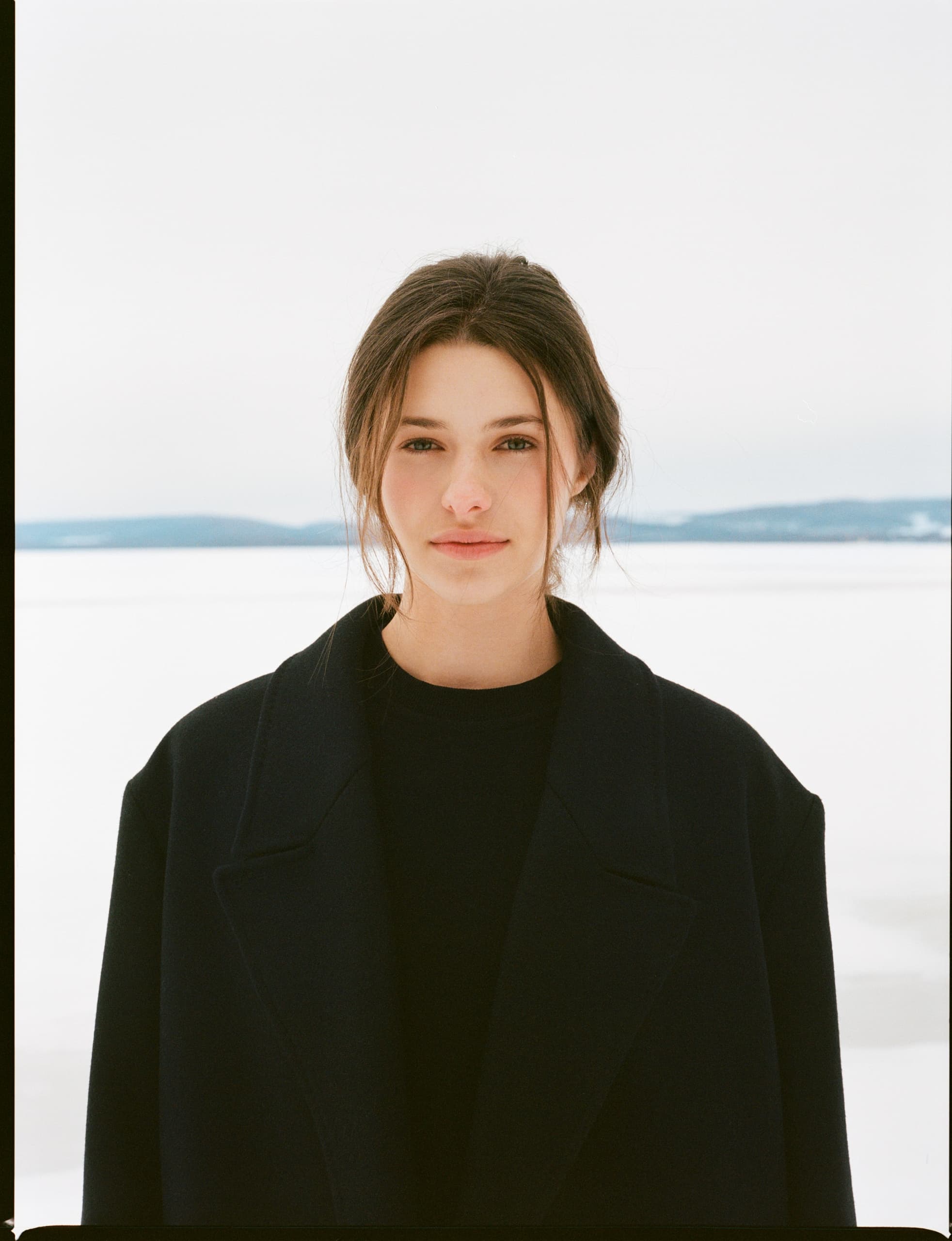 Woman in black coat with snowy landscape background.