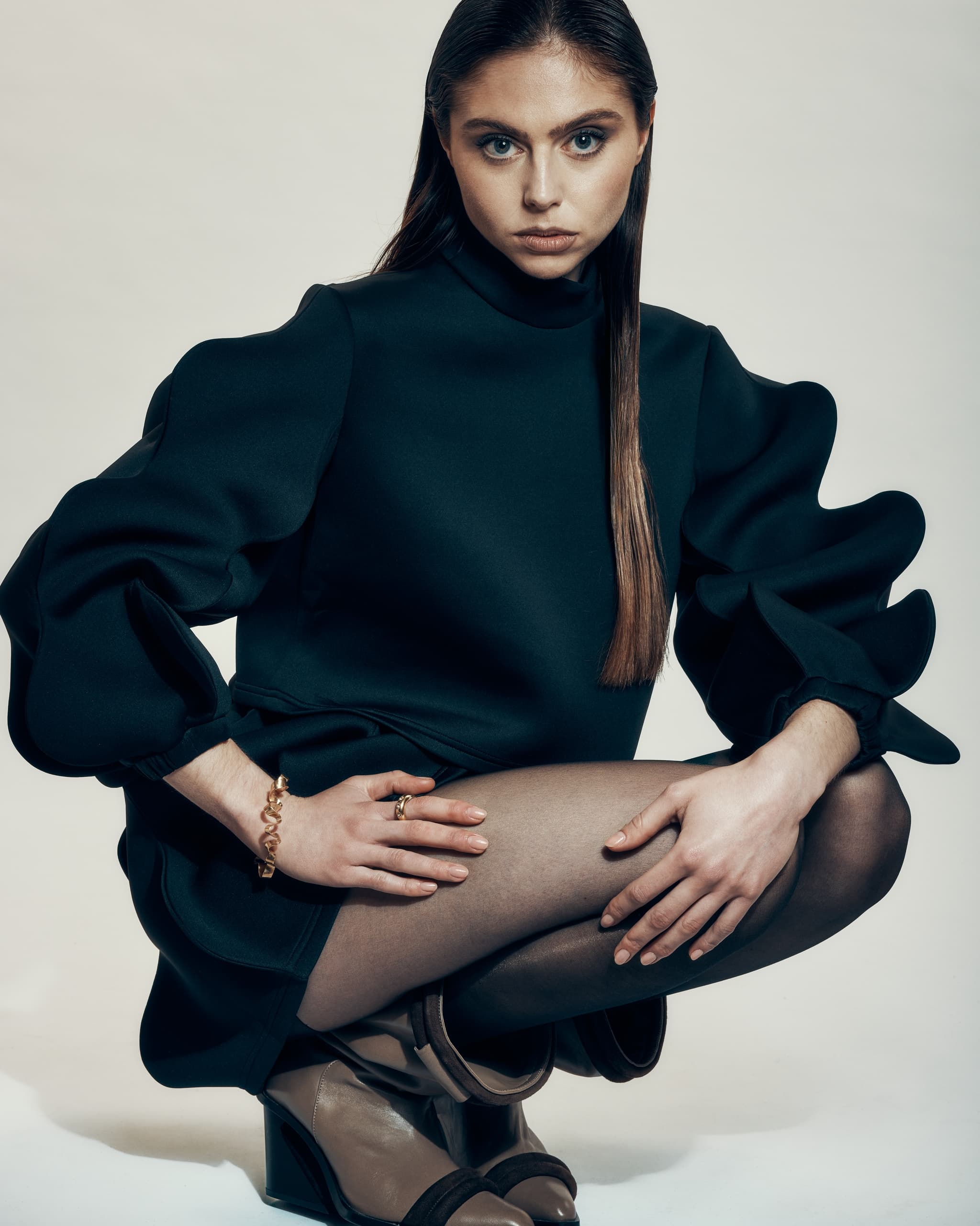 Fashion model in stylish black dress and boots, striking bold pose.
