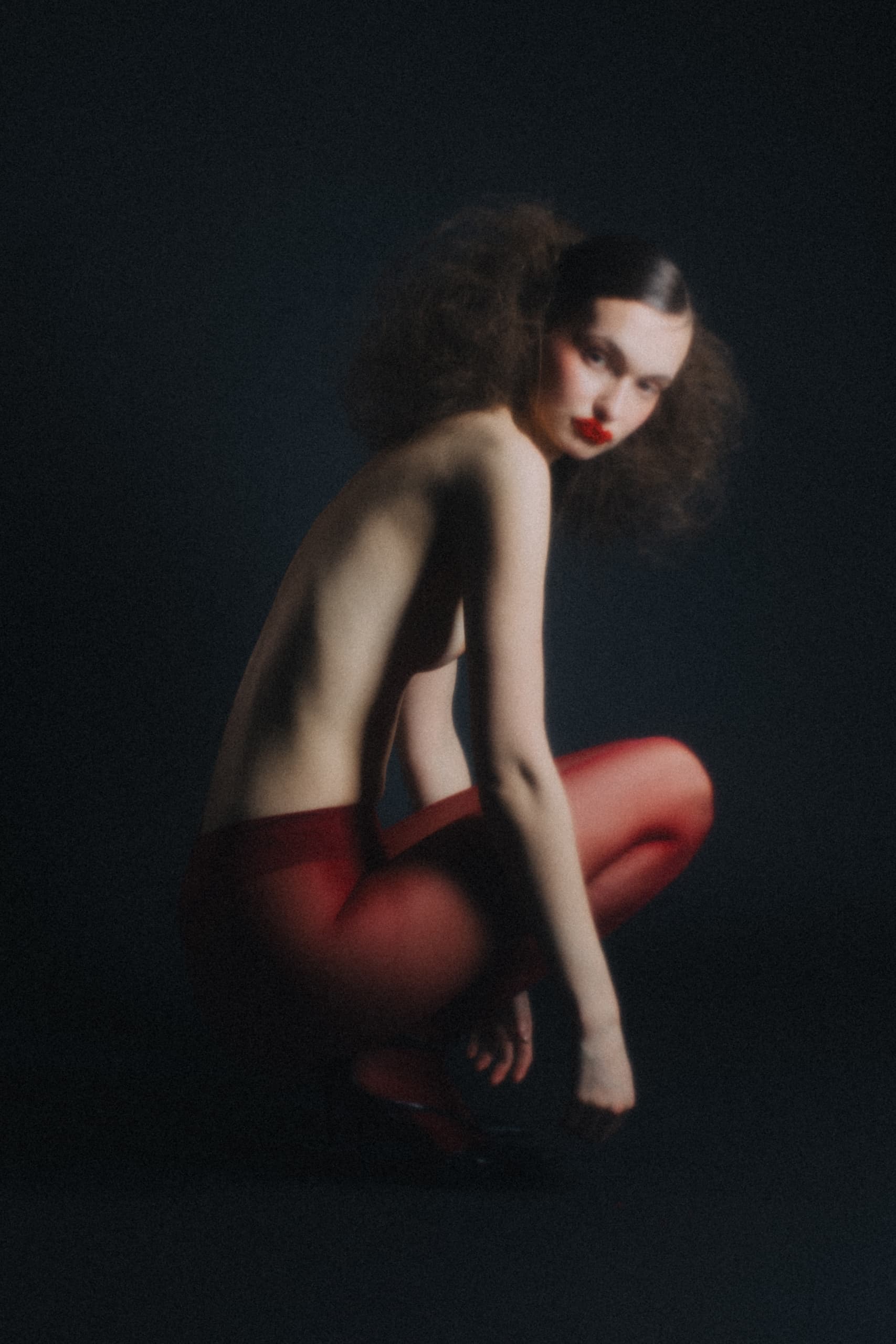 Artistic portrait of a woman in red tights with bold makeup on a dark background.