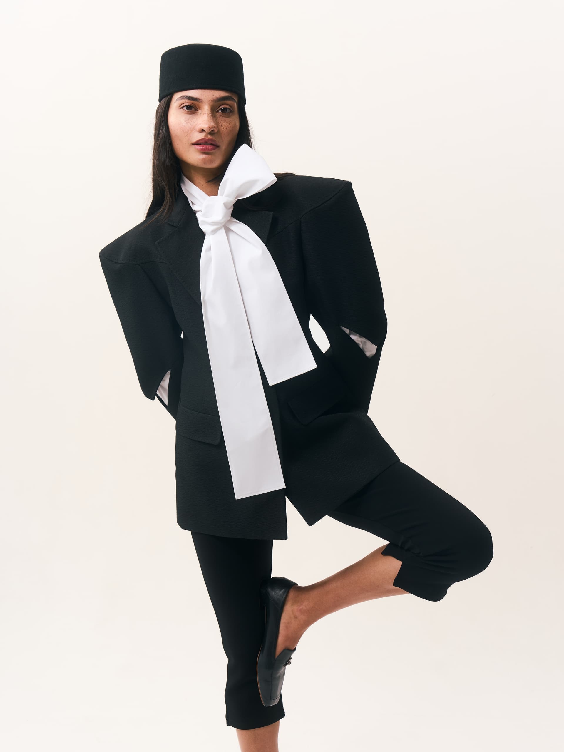 Fashion model in modern black outfit with white bow, striking a dynamic pose.