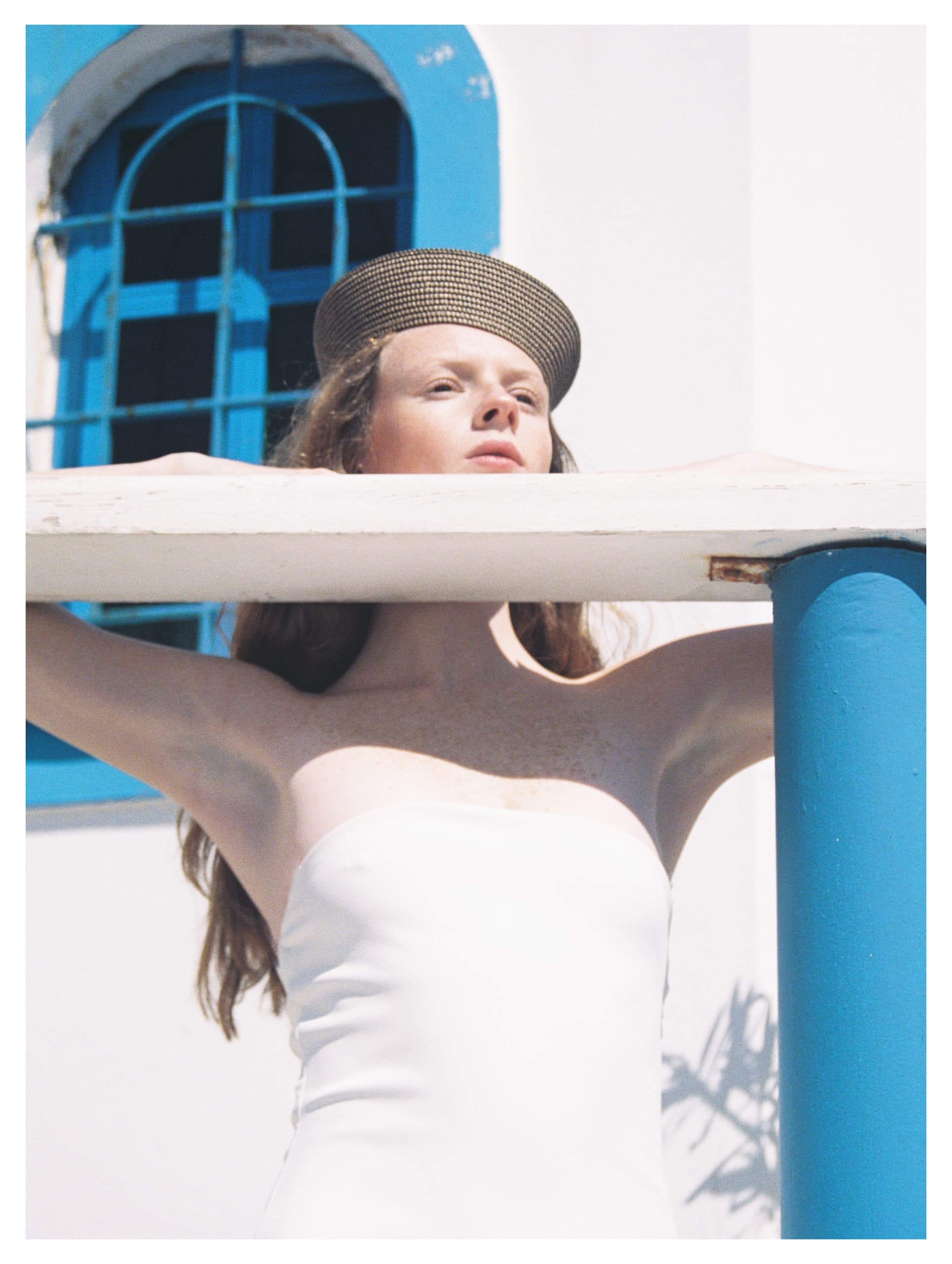 Person in sun hat stands by white building with blue accents.