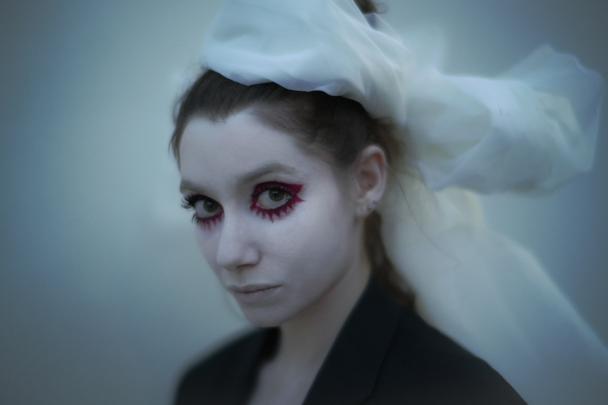 Woman with dramatic makeup and white headscarf in ethereal lighting.
