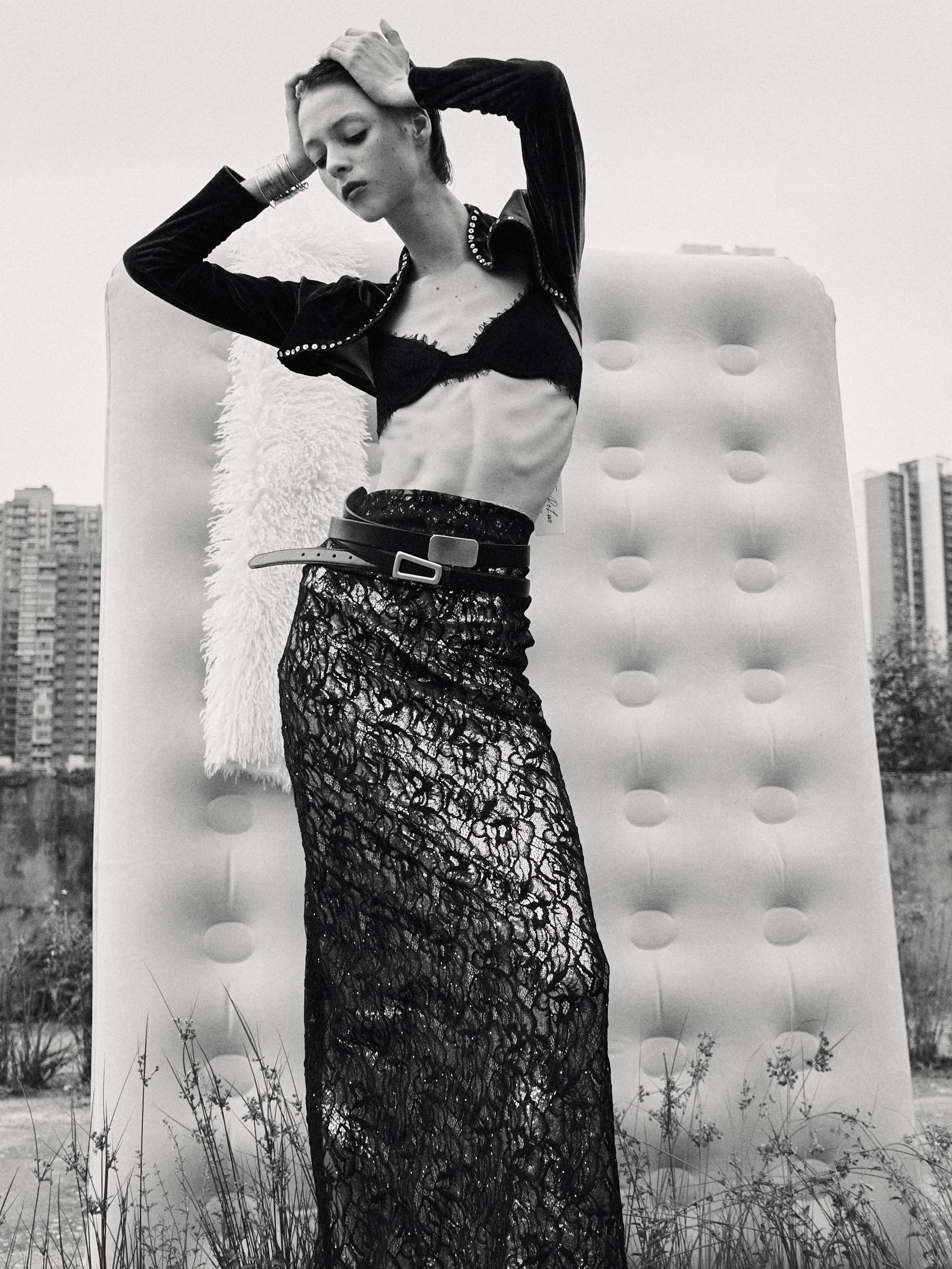Fashion model in lace skirt posing outdoors with modern cityscape background.