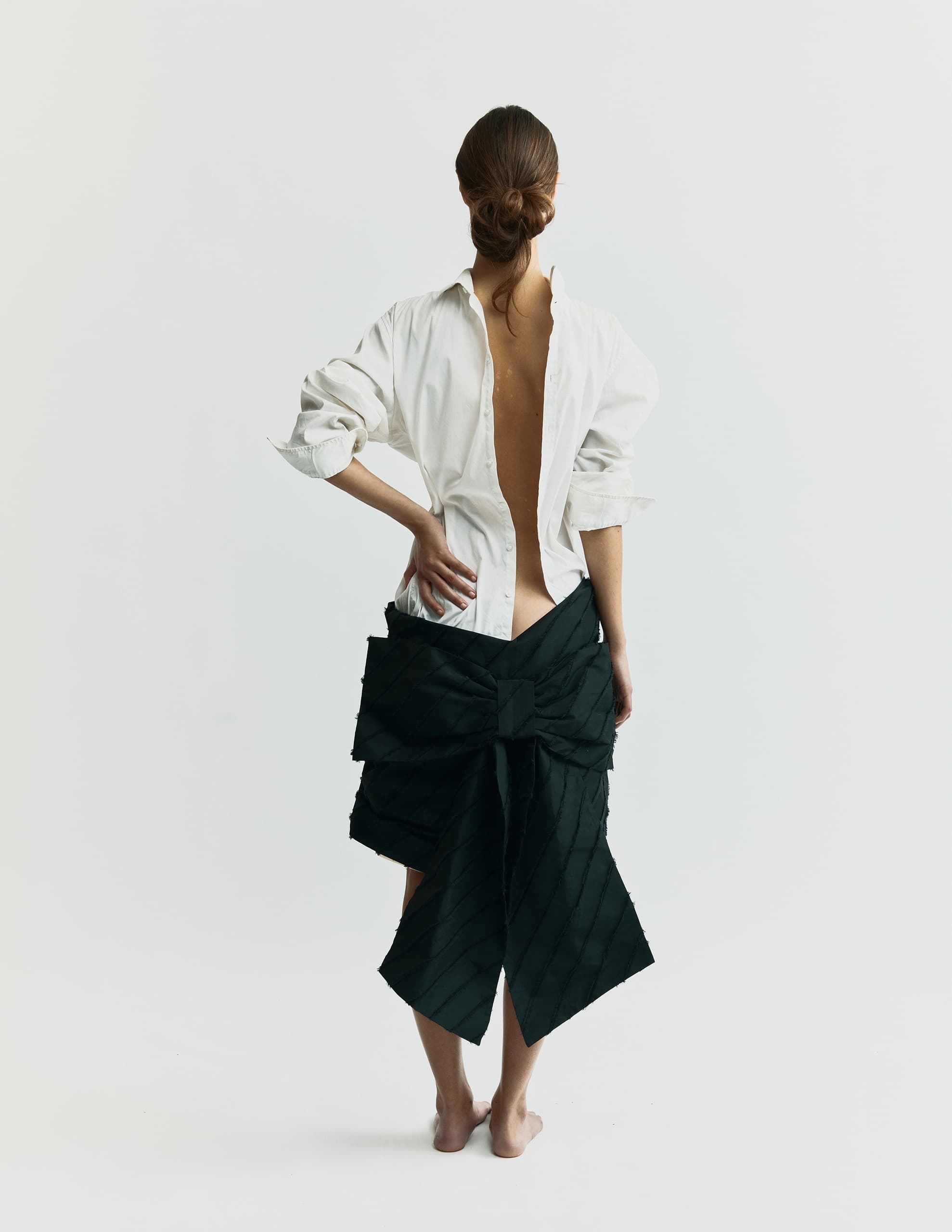 Fashion model in backless shirt with elegant black skirt and bow detail.