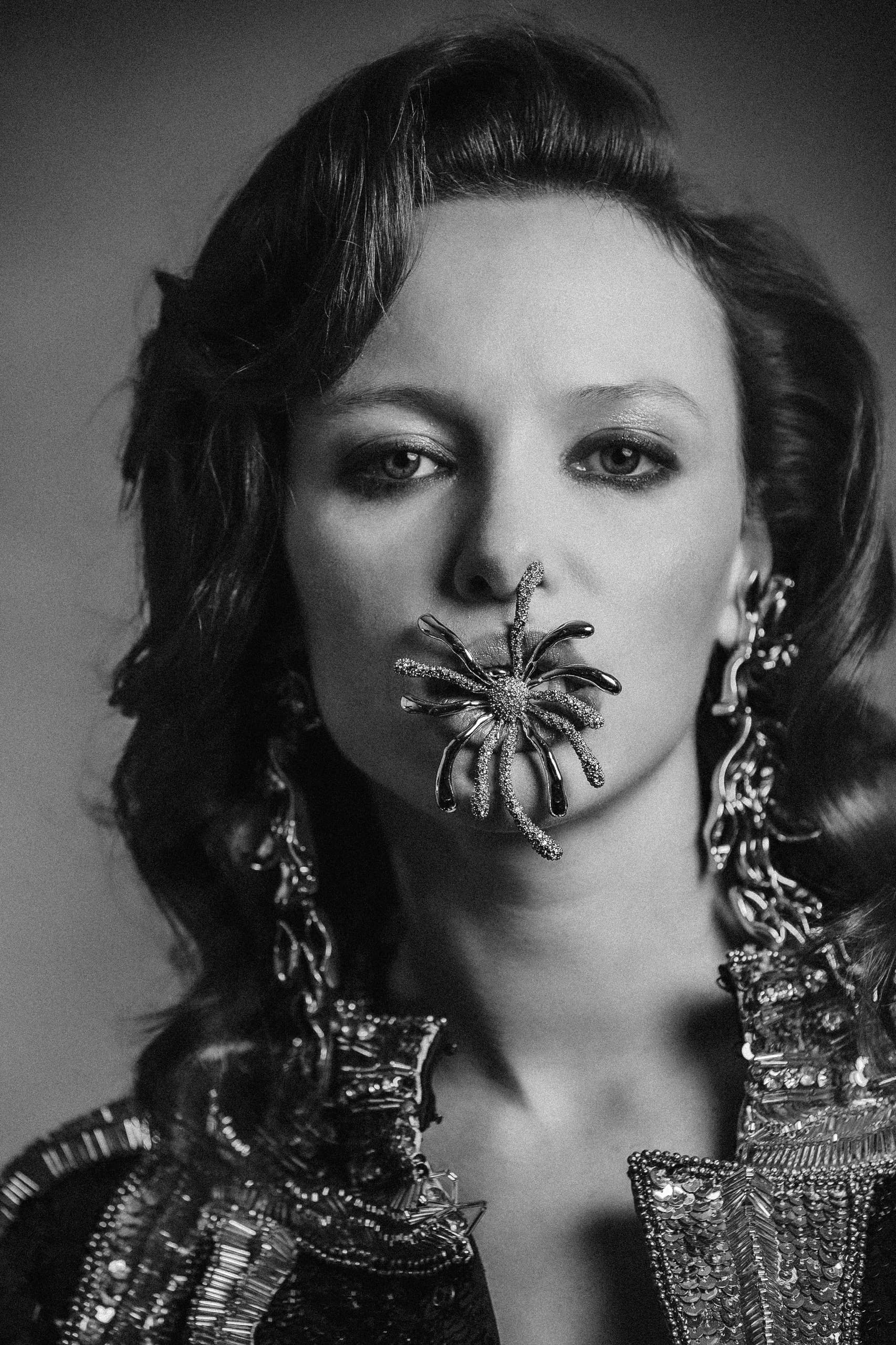 Black and white portrait of a woman with ornate jewelry and lip accessory.