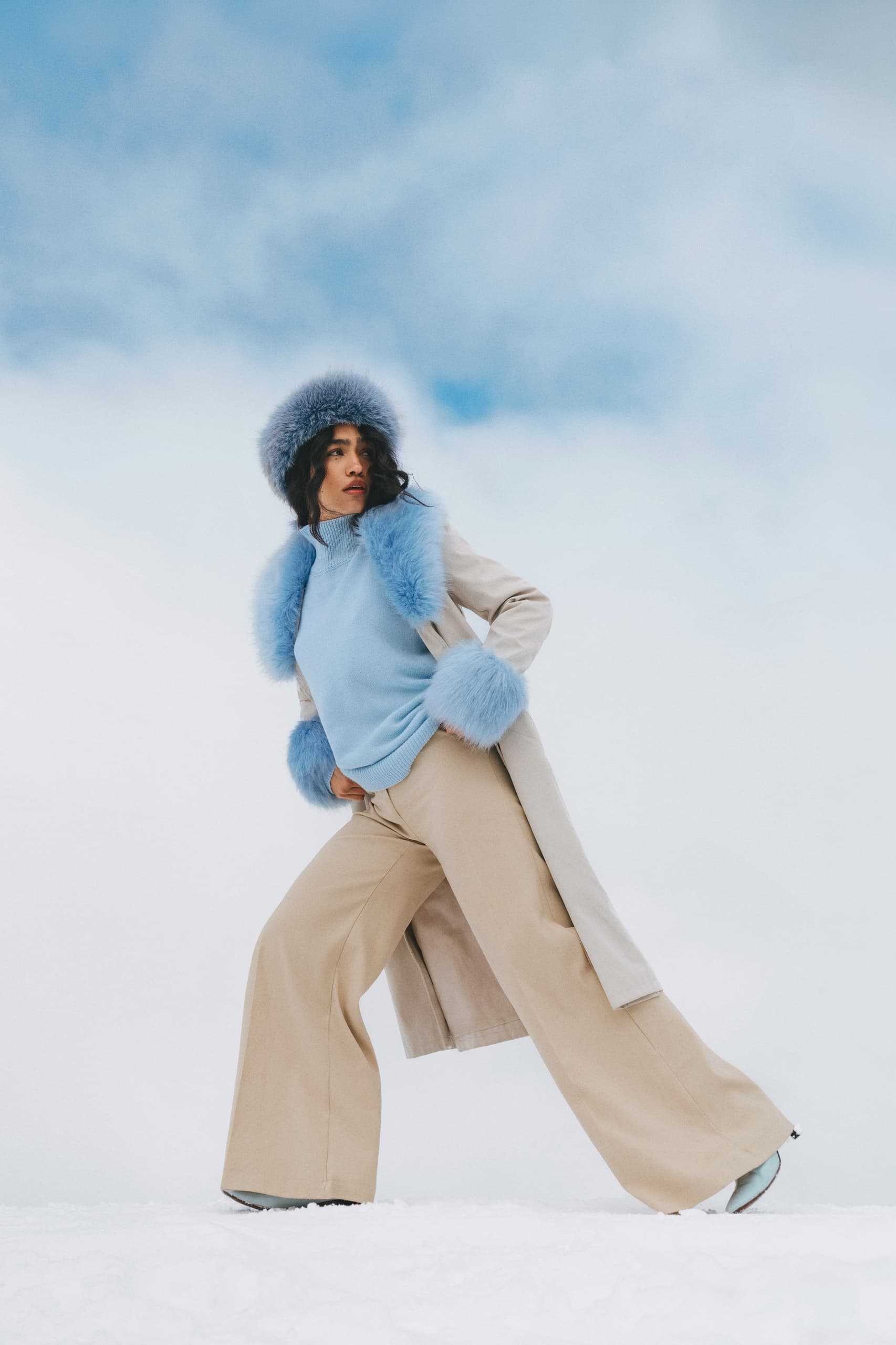 Woman in stylish winter outfit poses against a snowy background.
