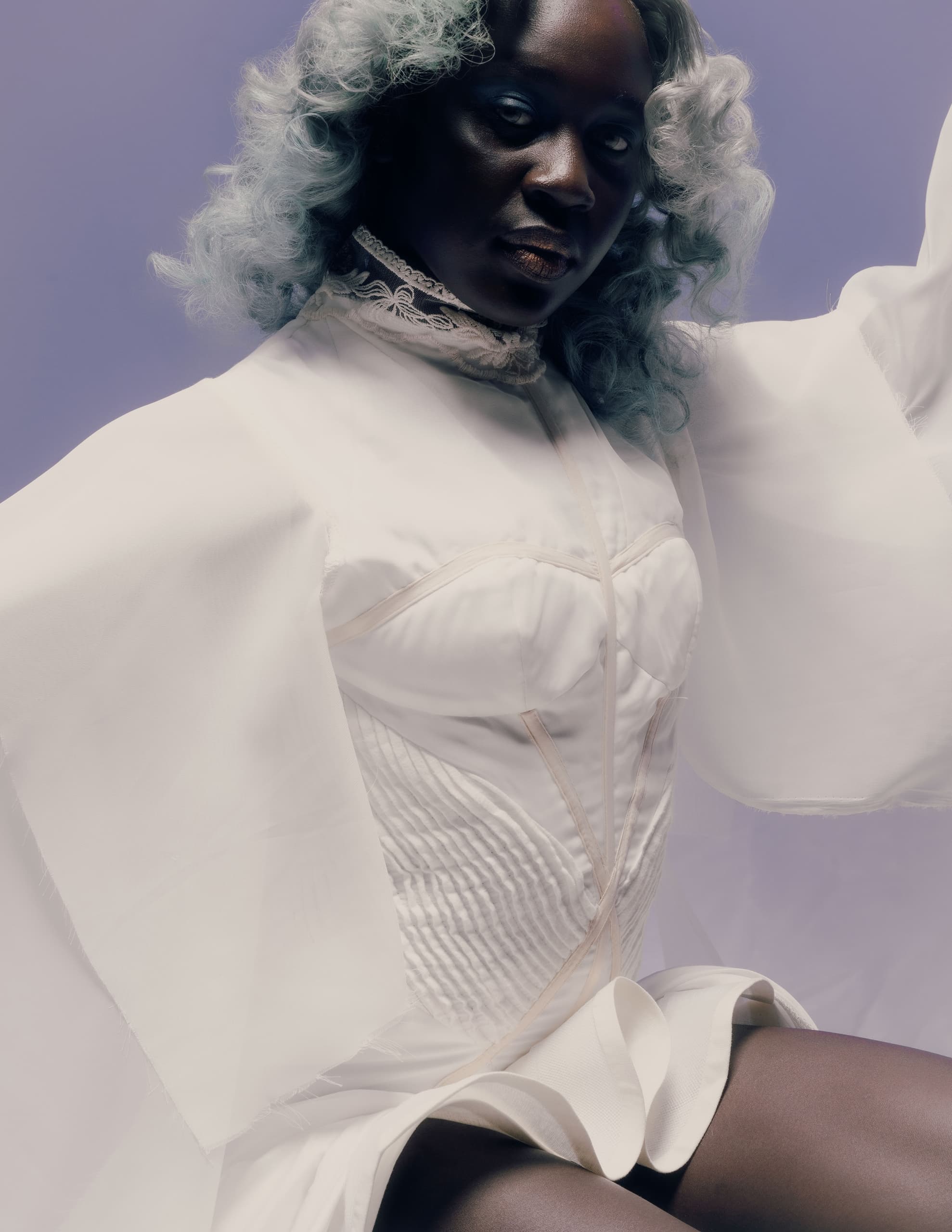 Fashion model in elegant white dress with curly hair against a soft purple background.