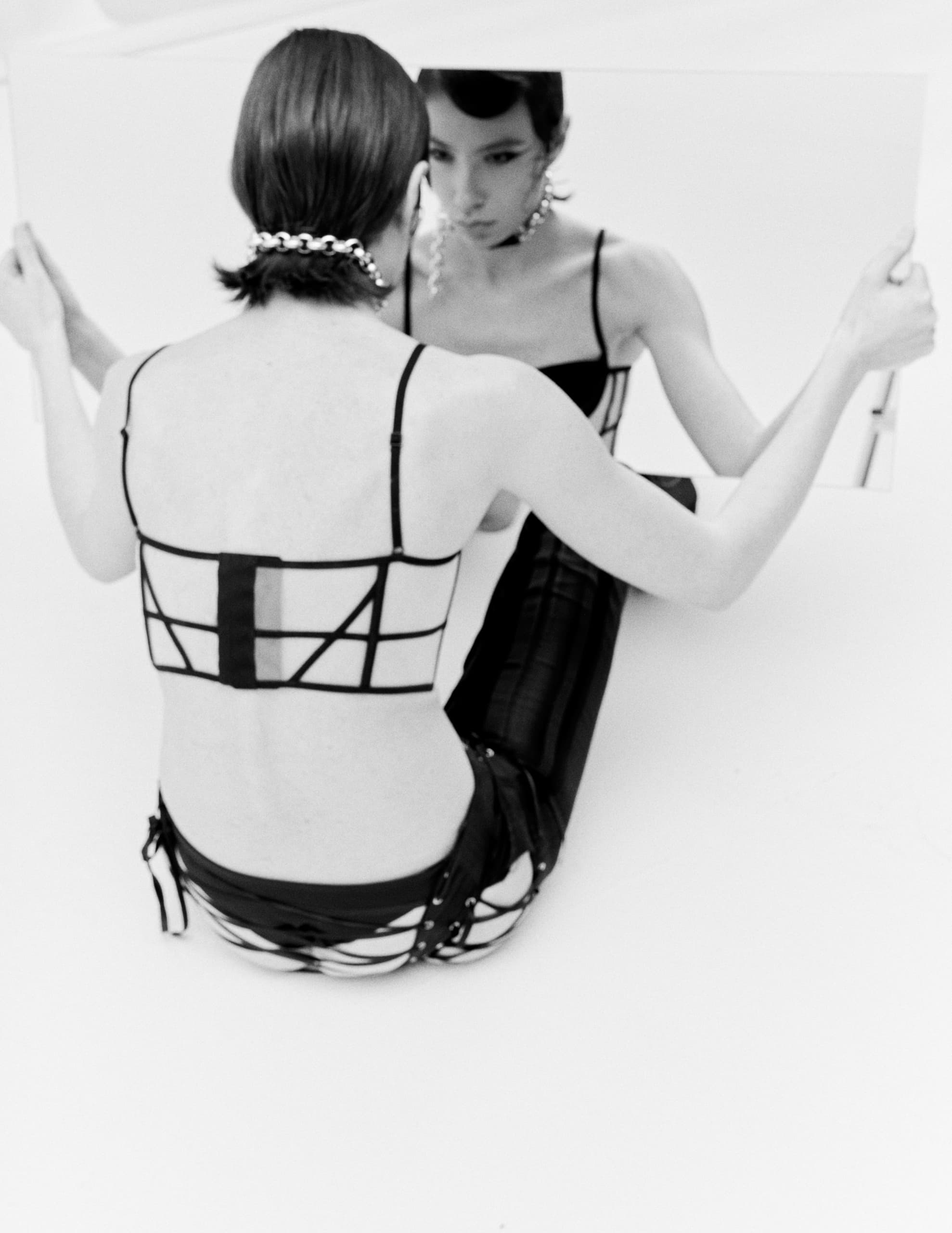 Person in stylish outfit holding a mirror, reflecting thoughtful expression.